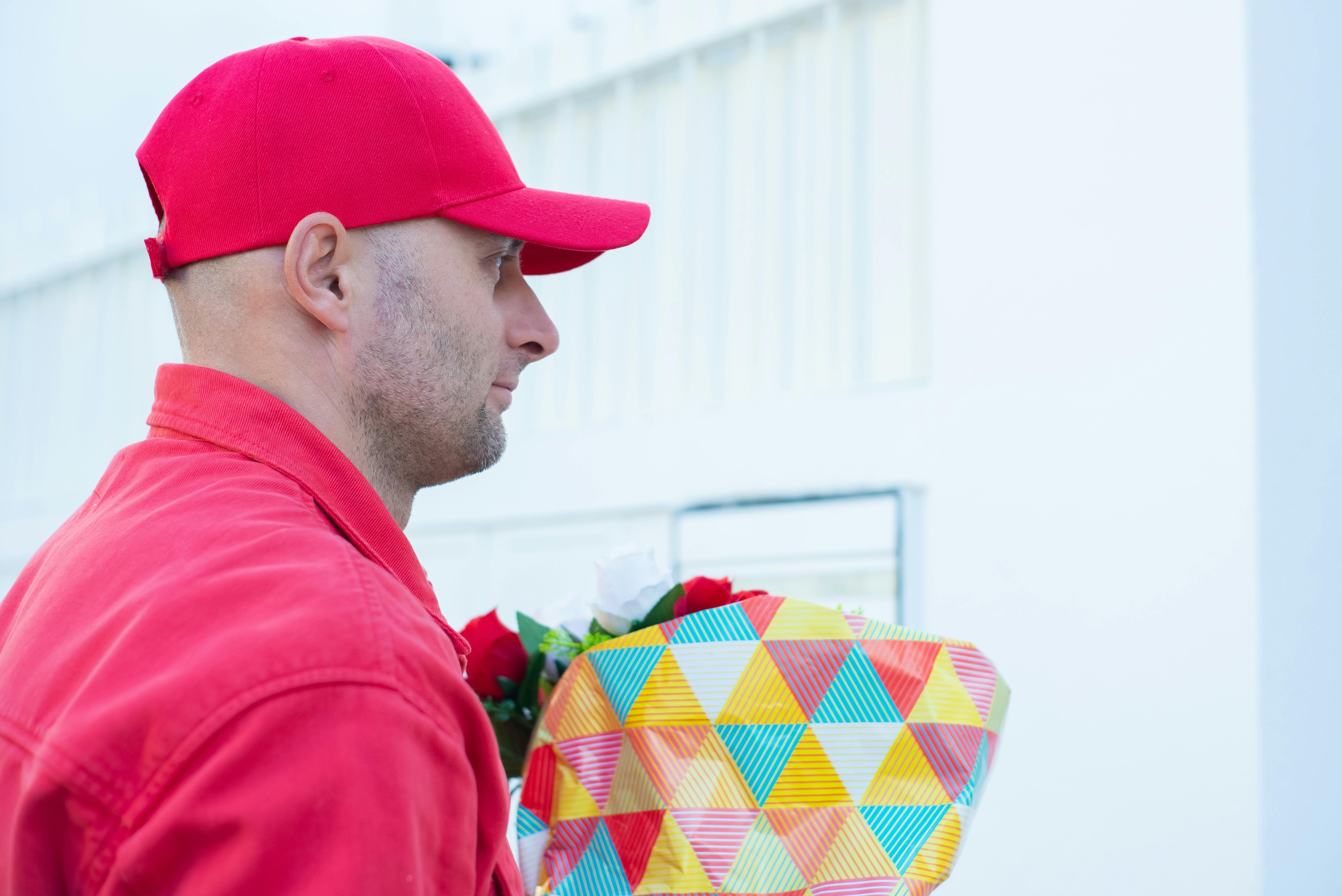 A Man Wearing Red Cap and Jacket while Holding Flowers