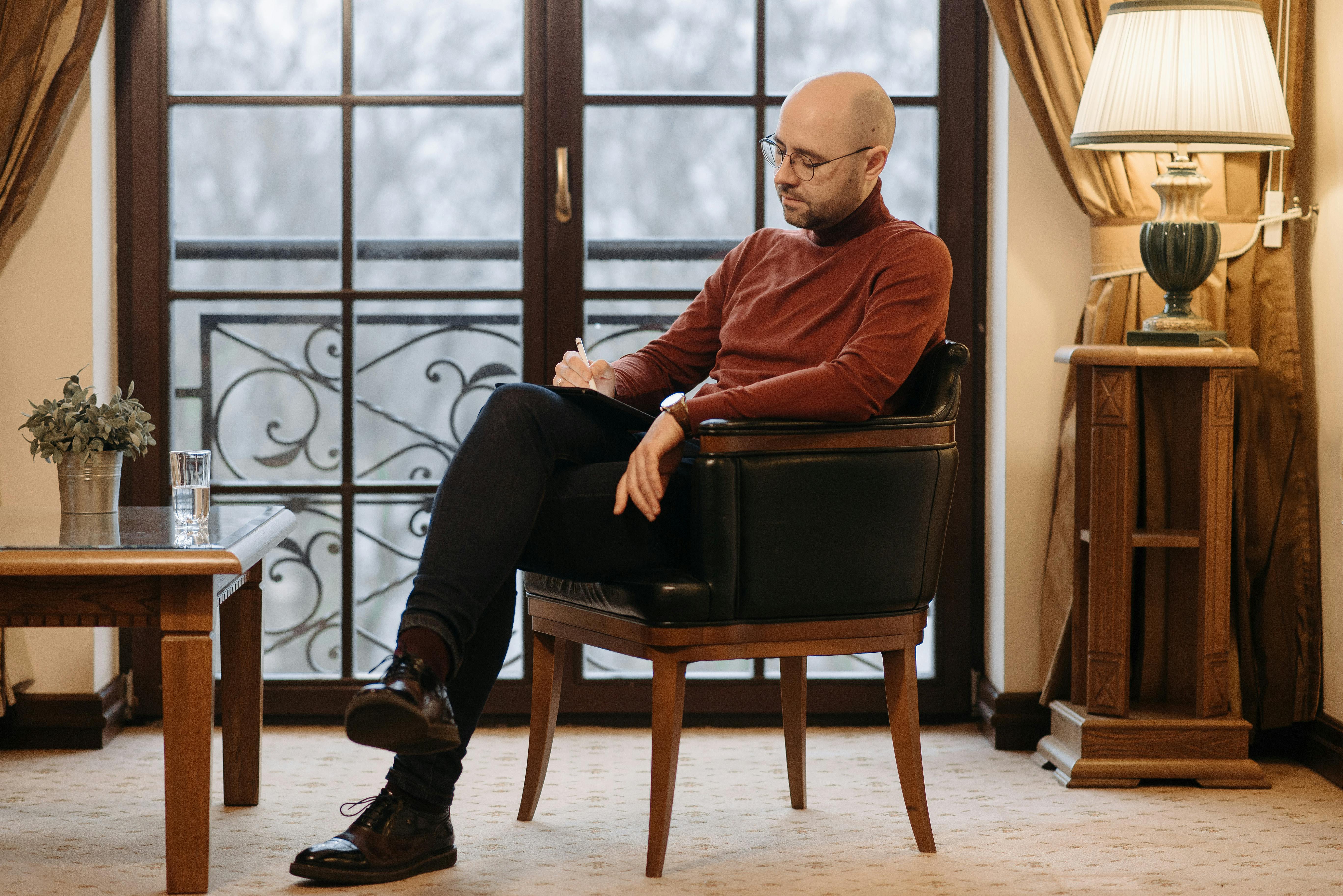 A Man Sitting on Black Leather Chair with Wooden Feet