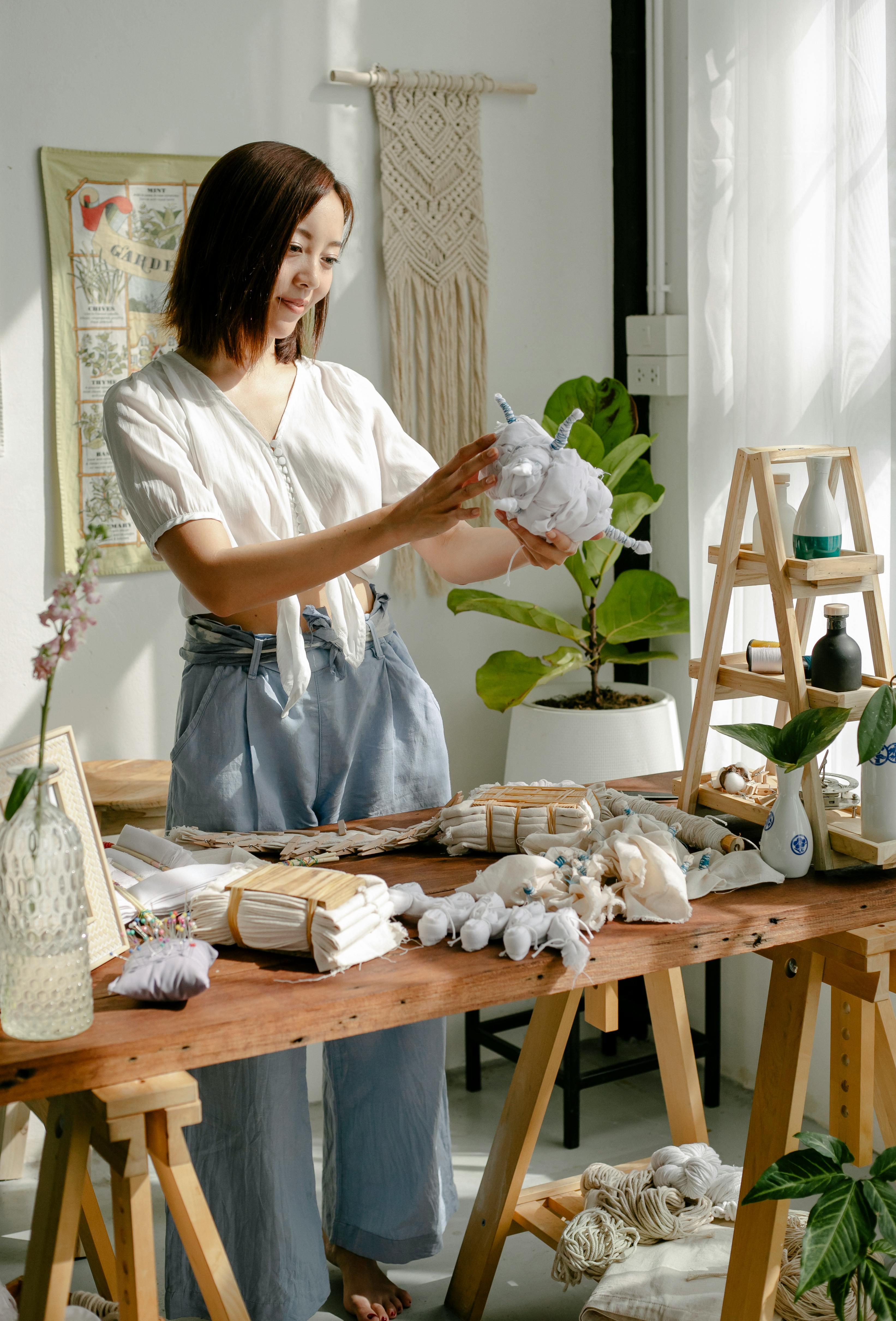 Creative young ethnic female dressmaker tying cotton fabrics before dyeing clothes in traditional Japanese shibori technique in workshop