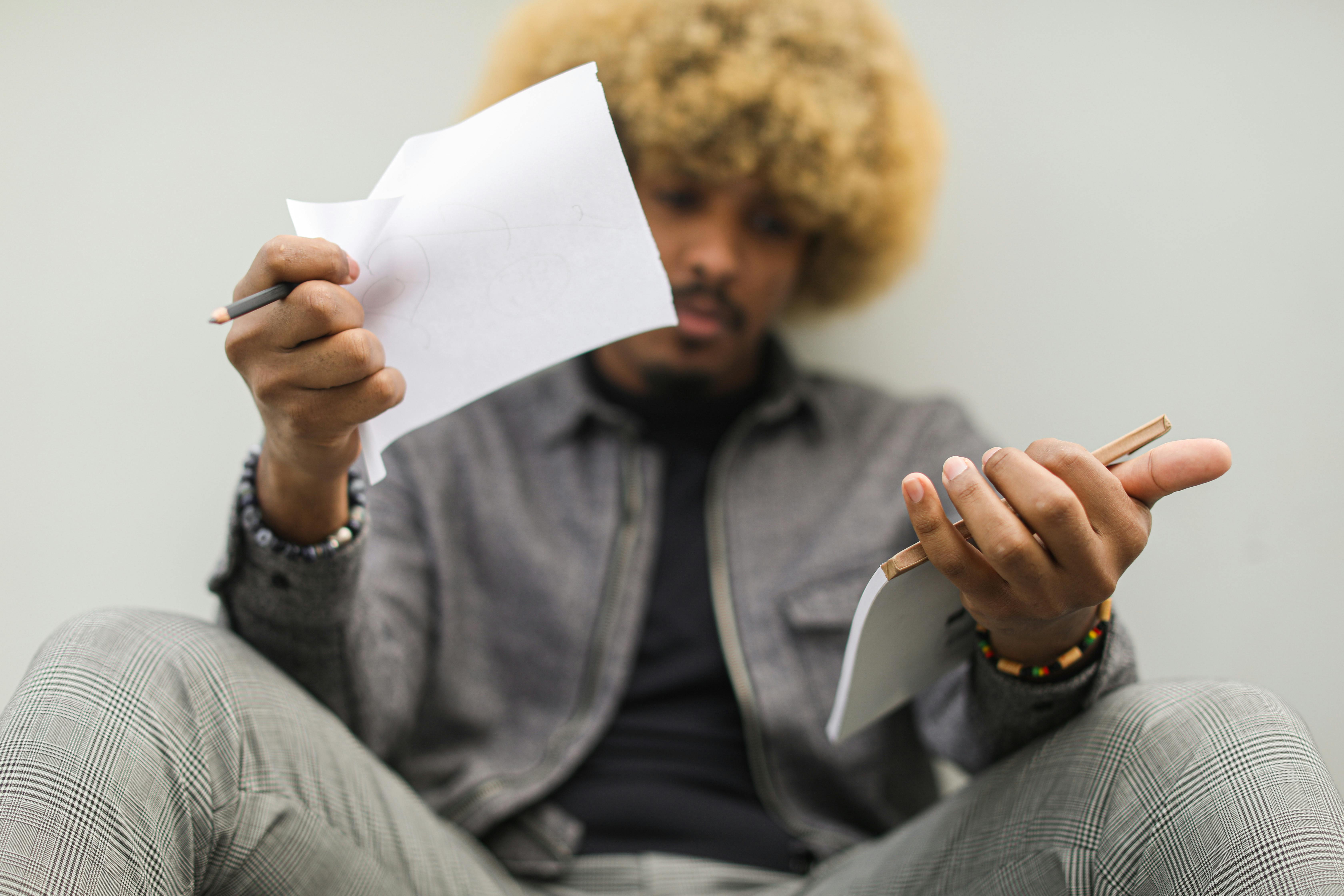 Colored Hair Man Holding a Piece of Paper and a Notebook