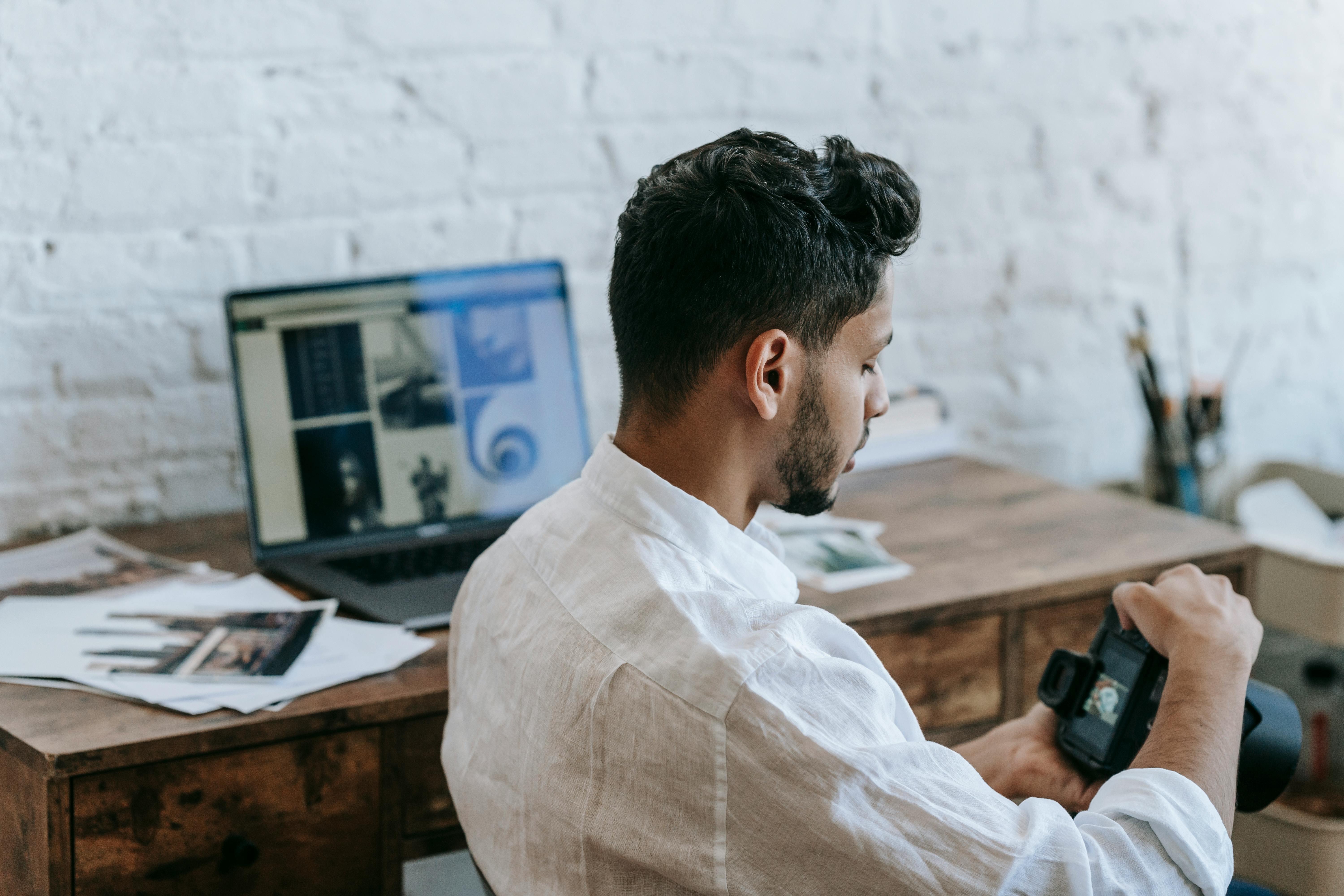 Attentive ethnic man using photo camera in light room