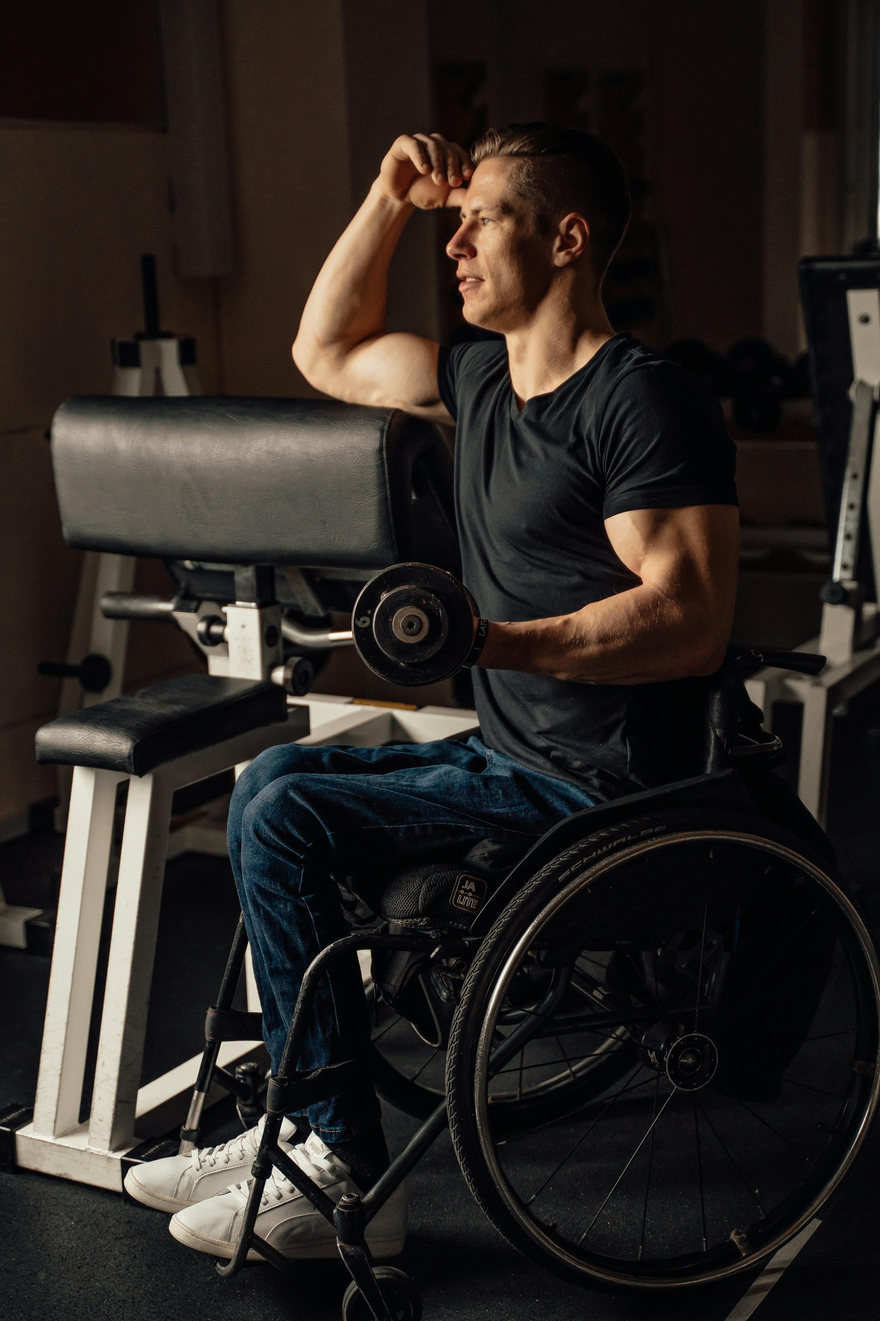 Man in Black Shirt Sitting on a Wheelchair while Holding a Dumbbell