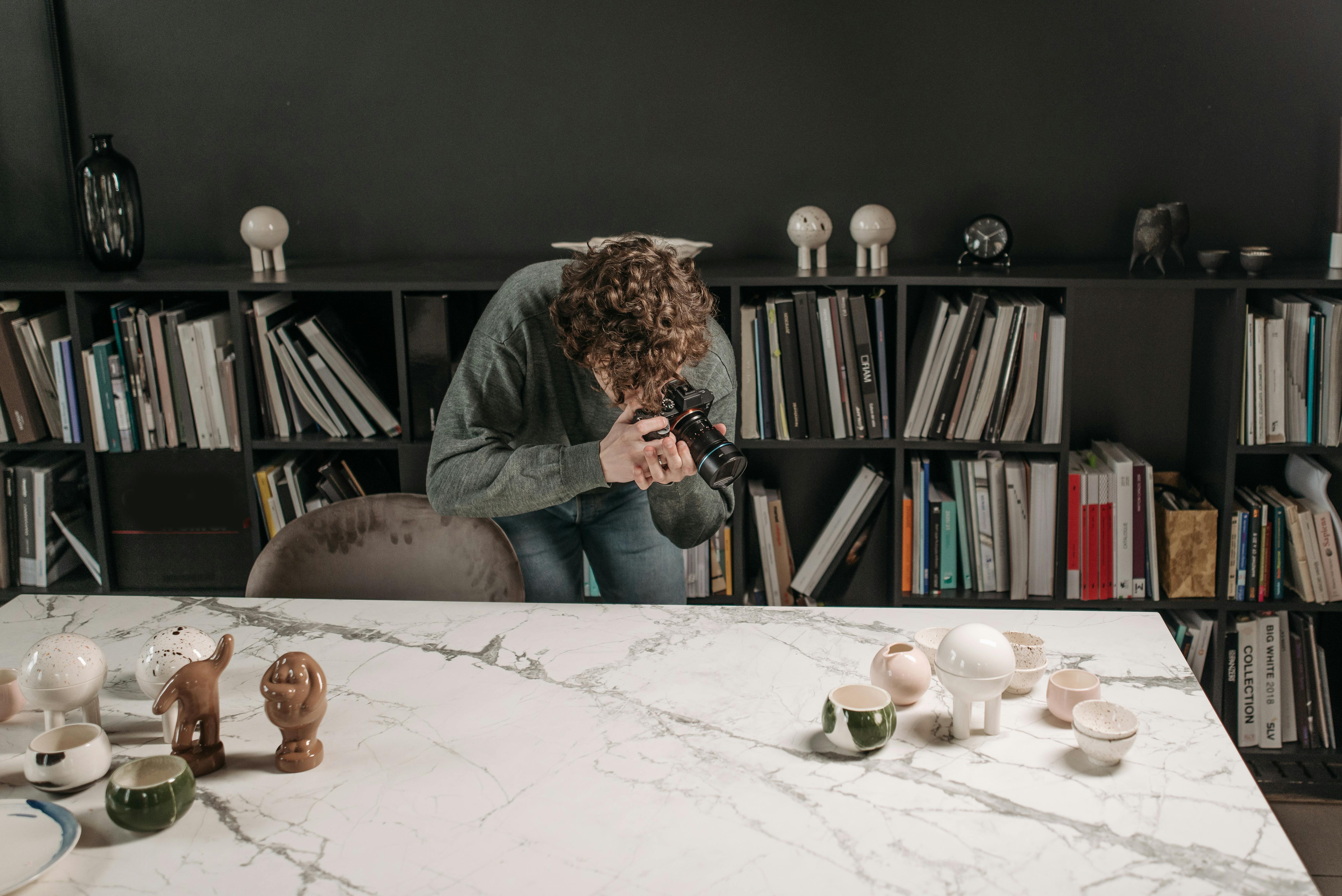 Man Taking Picture of Ceramic Products on Table