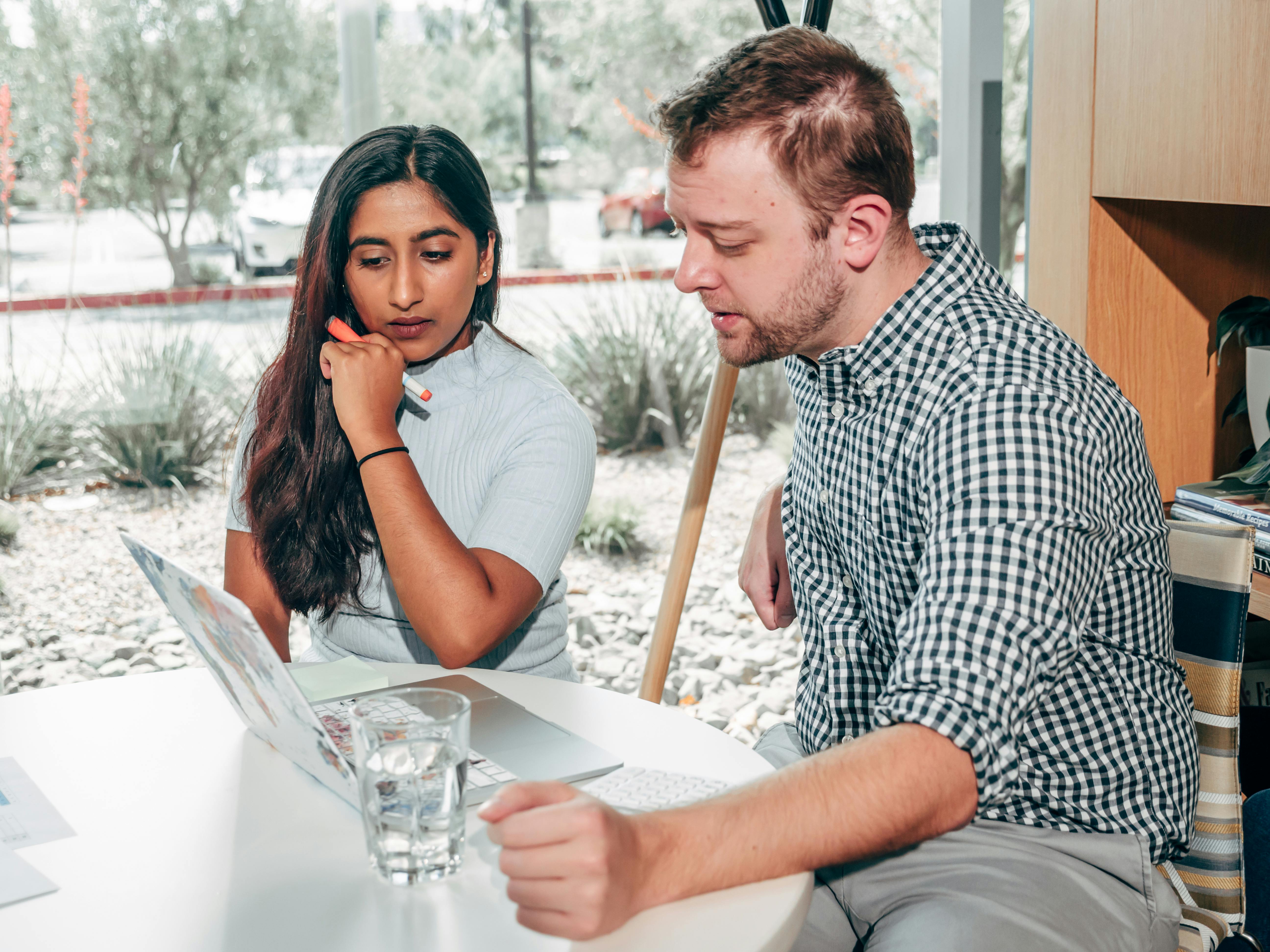 A Man and a Woman Sitting at the Table While Looking at the Laptop