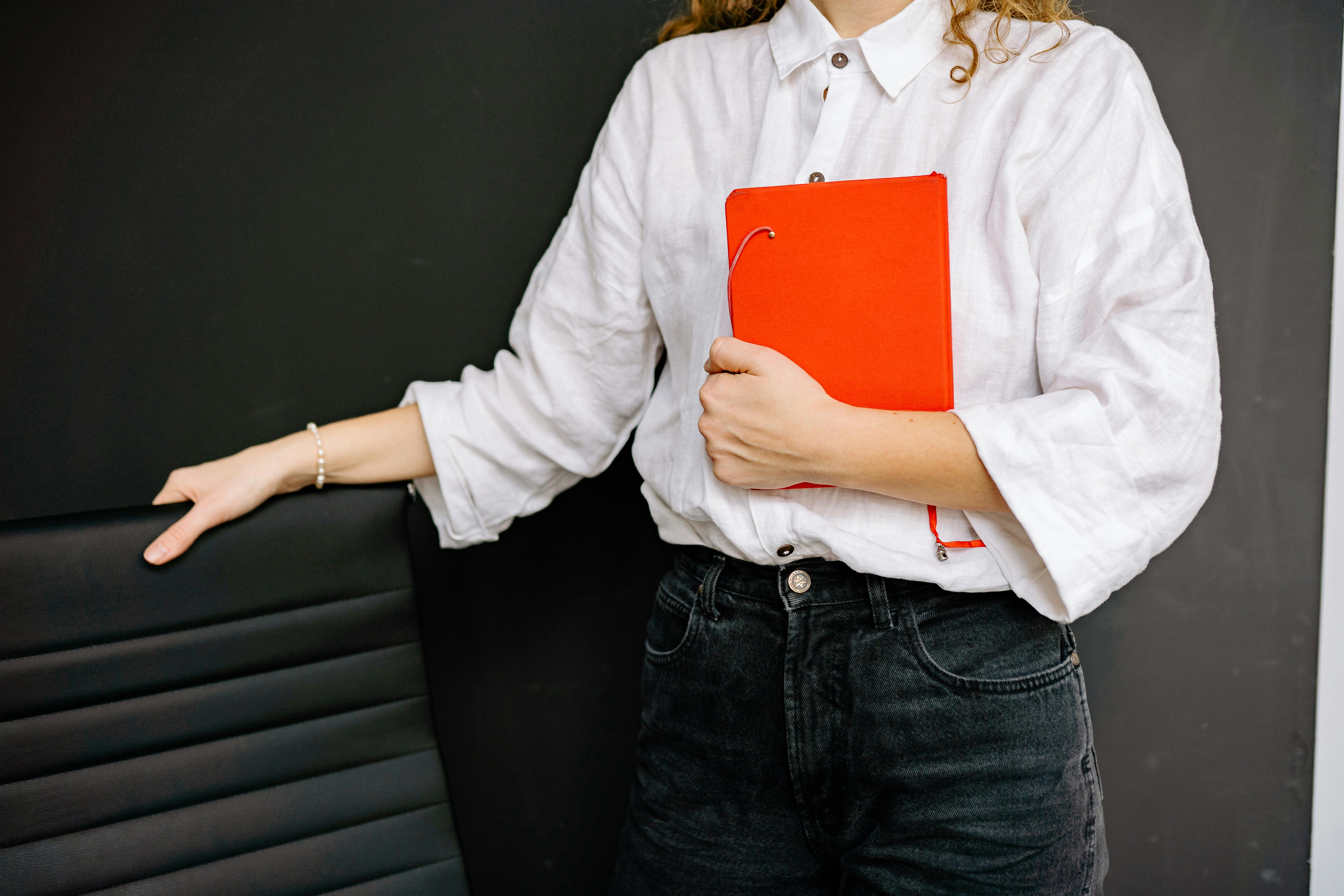 A Woman in White Long Sleeve Shirt Holding Red Notebook