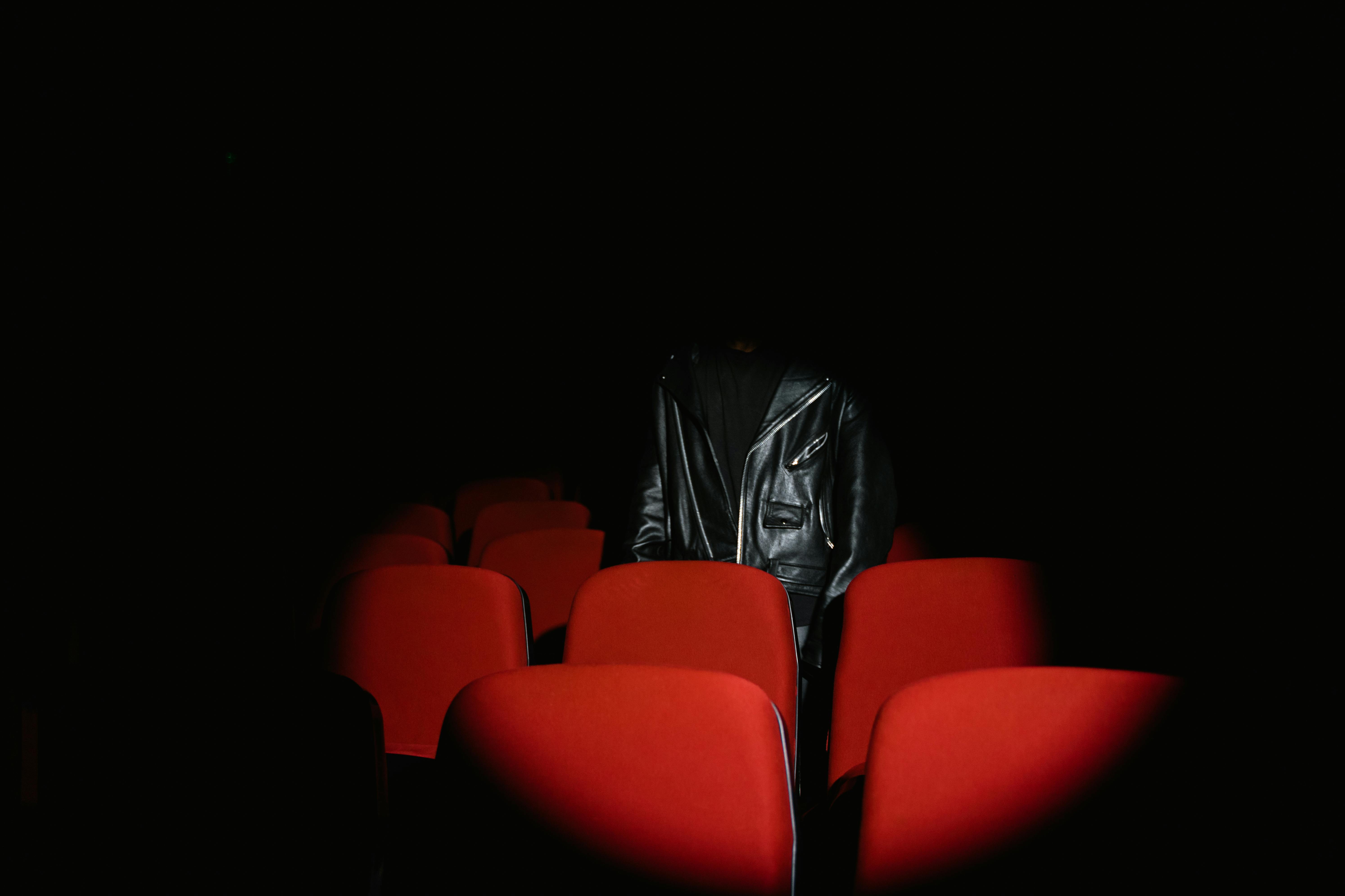 Person in Black Leather Jacket Standing Behind Red Theater Seat