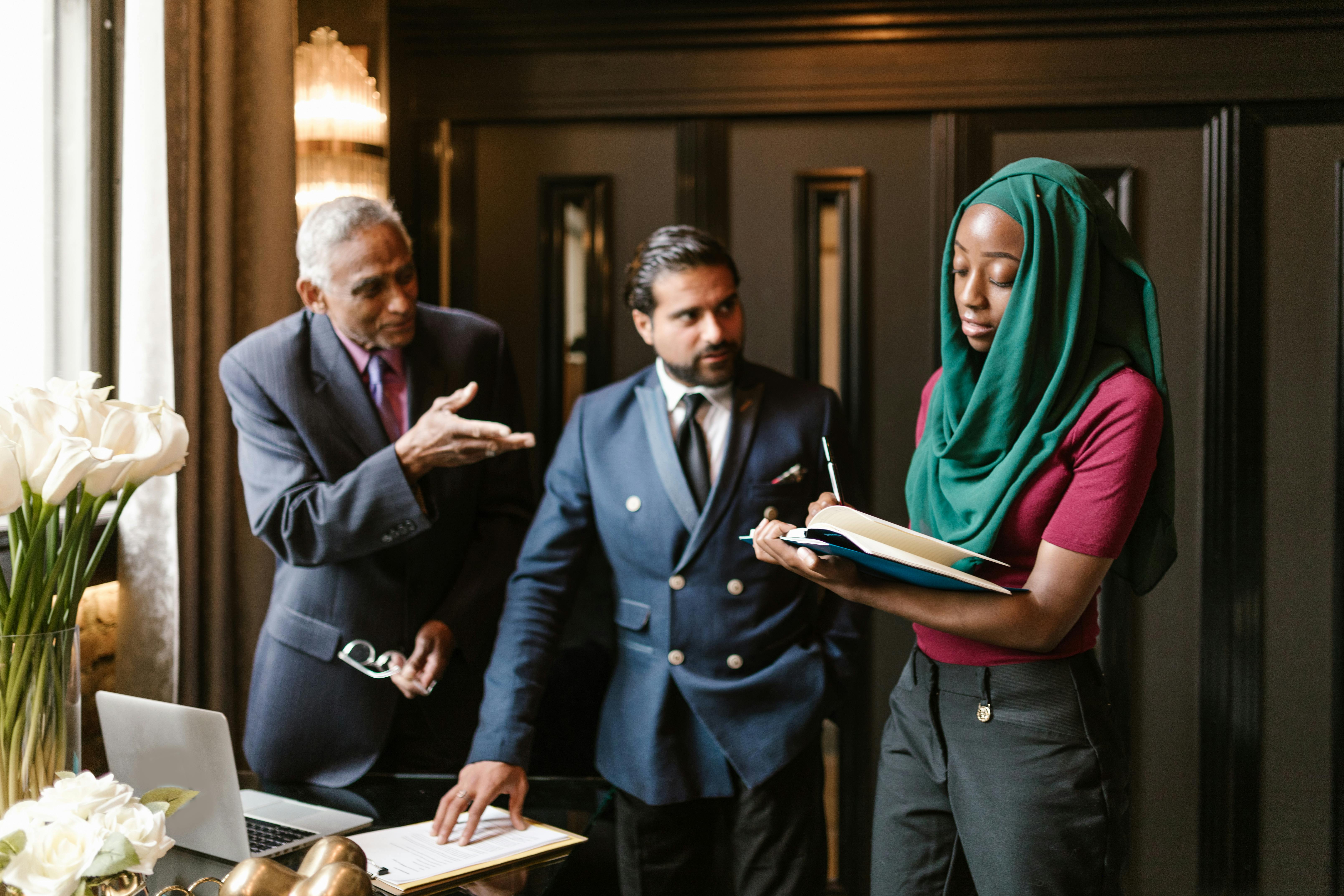 A Woman Wearing Hijab Taking Notes while Listening to the People Beside Her
