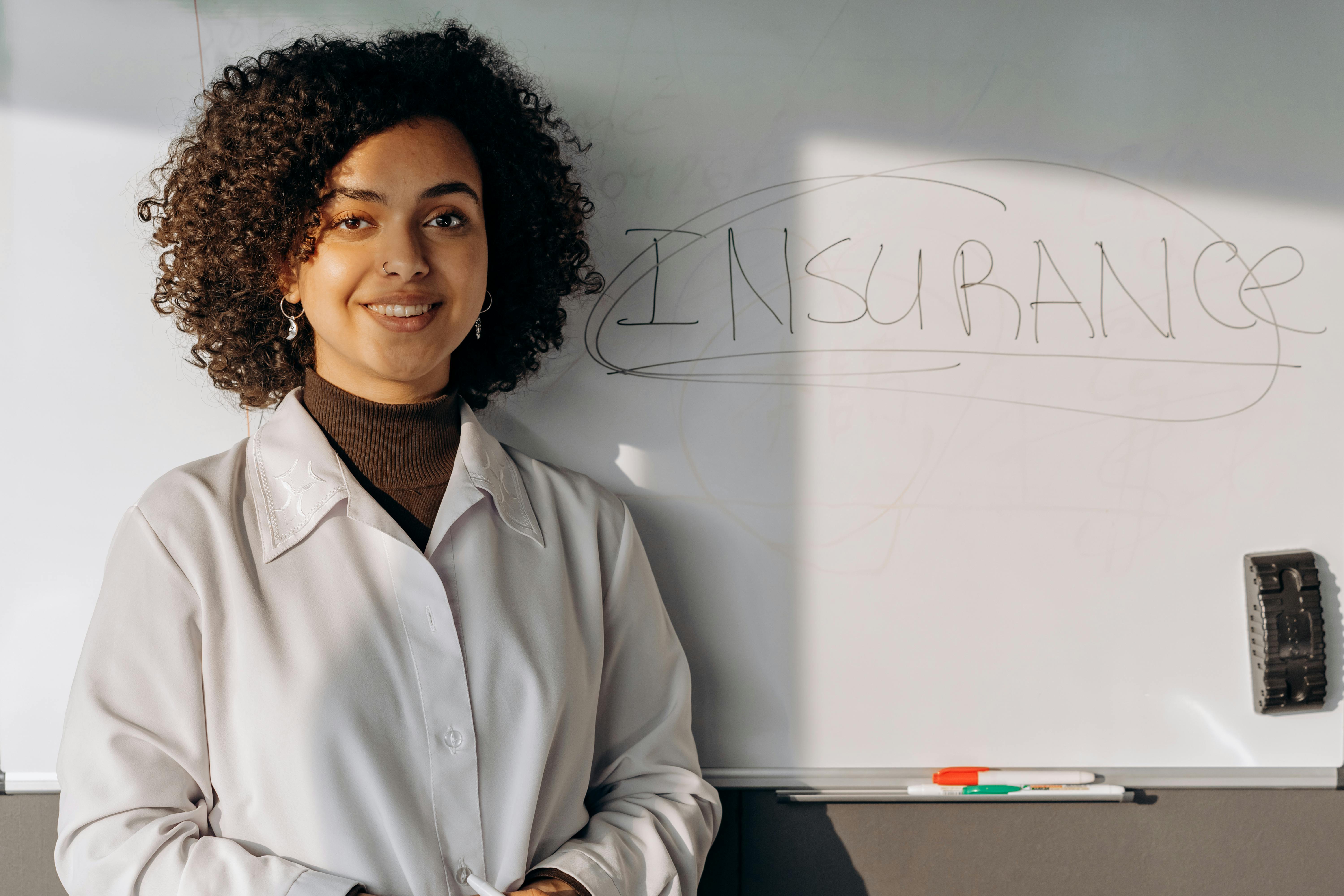 A Woman in White Long Sleeves Smiling while Standing Near the Whiteboard