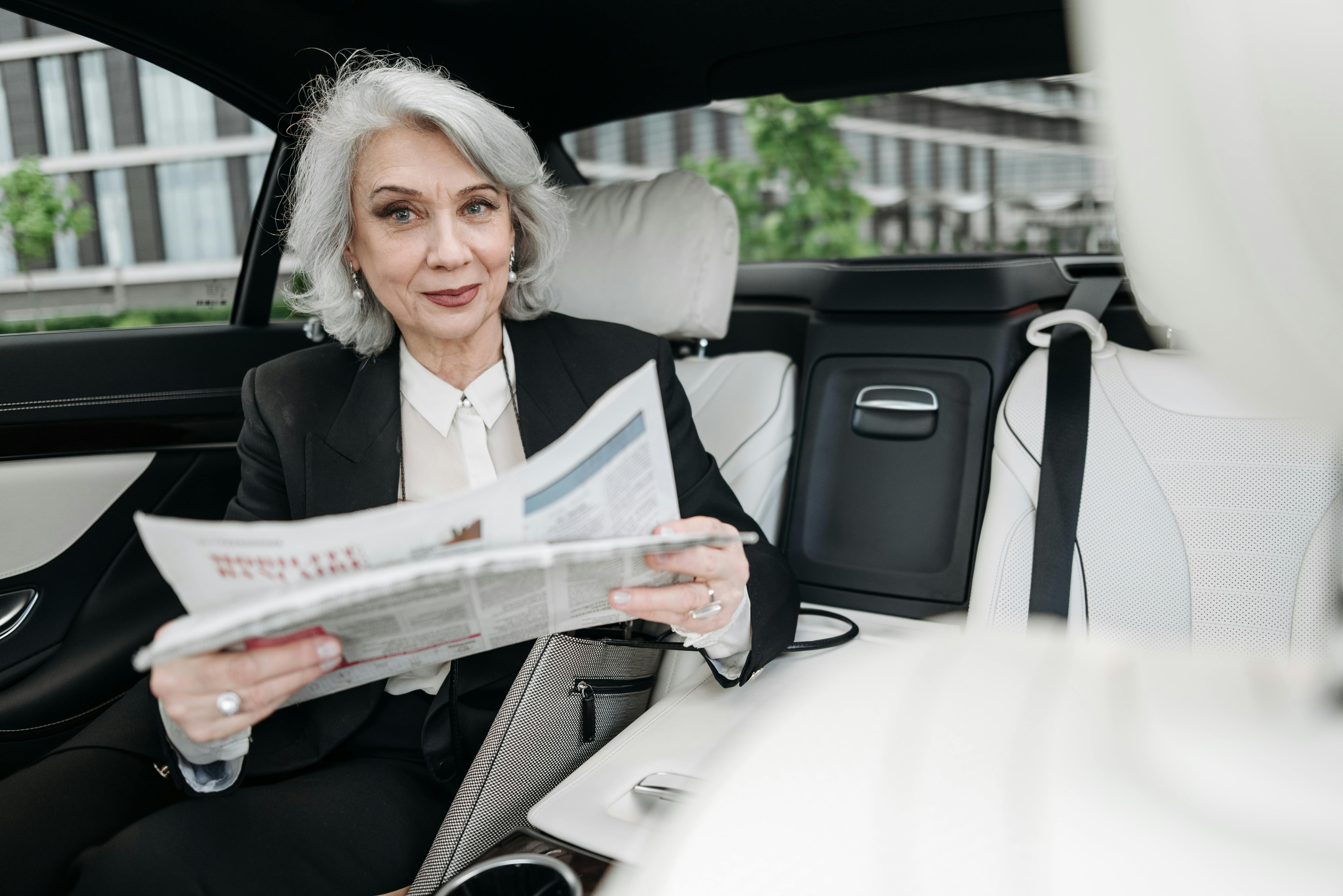 Woman in Black Blazer Holding Newspaper while Sitting inside the Car