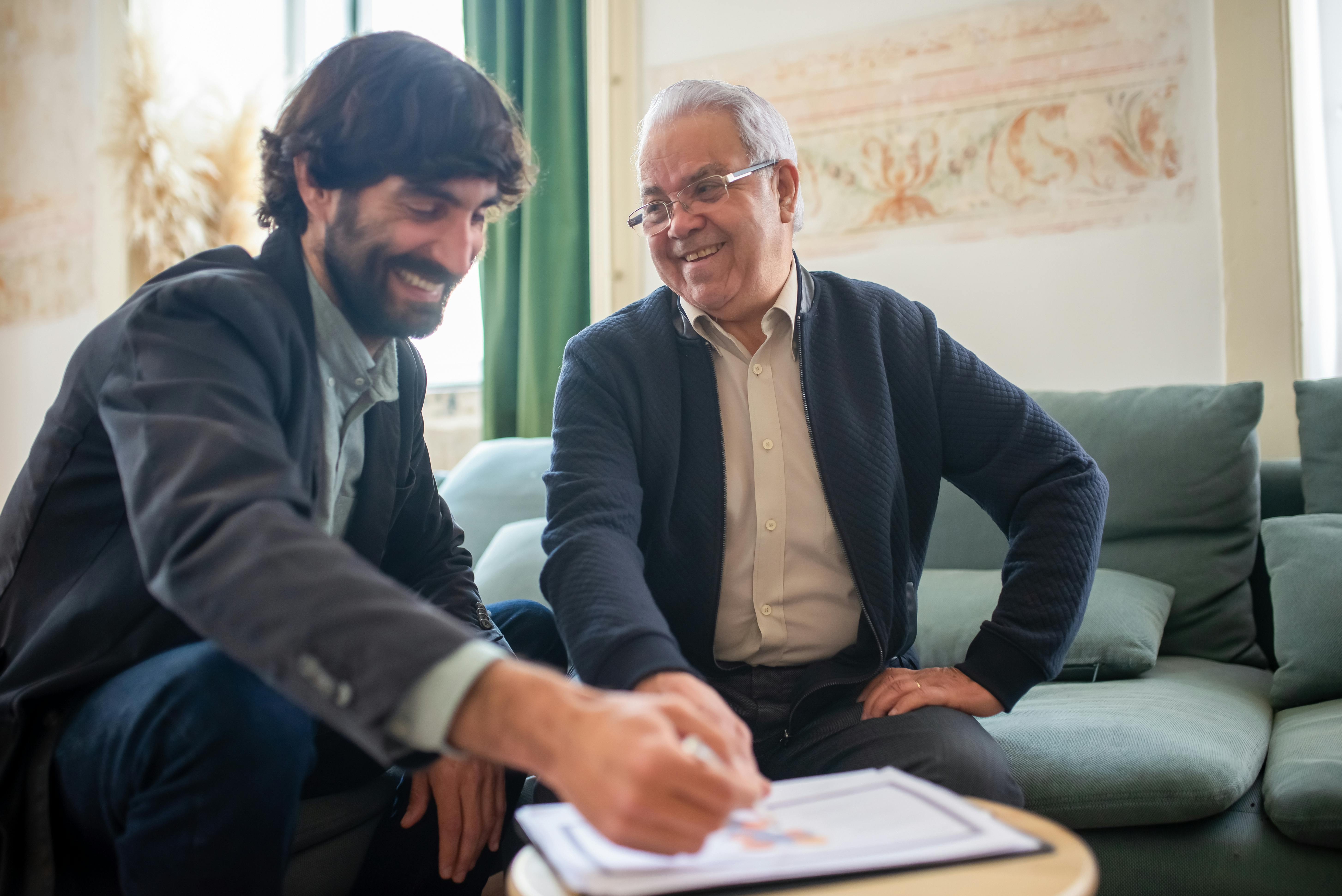 Two Men Smiling While Discussing Paperwork on a Wooden Table