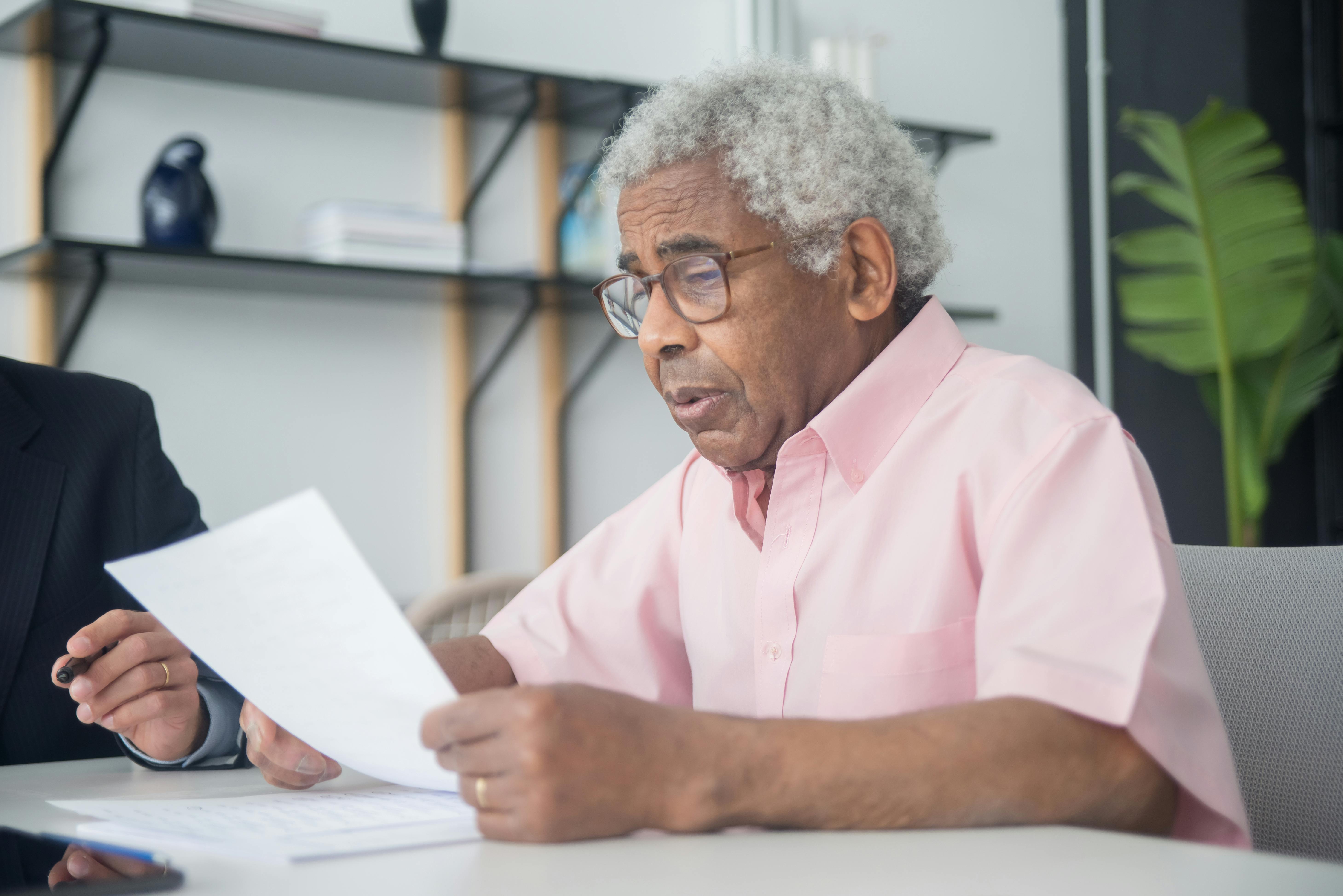 A Man in Pink Button-Up Shirt Reading a Document