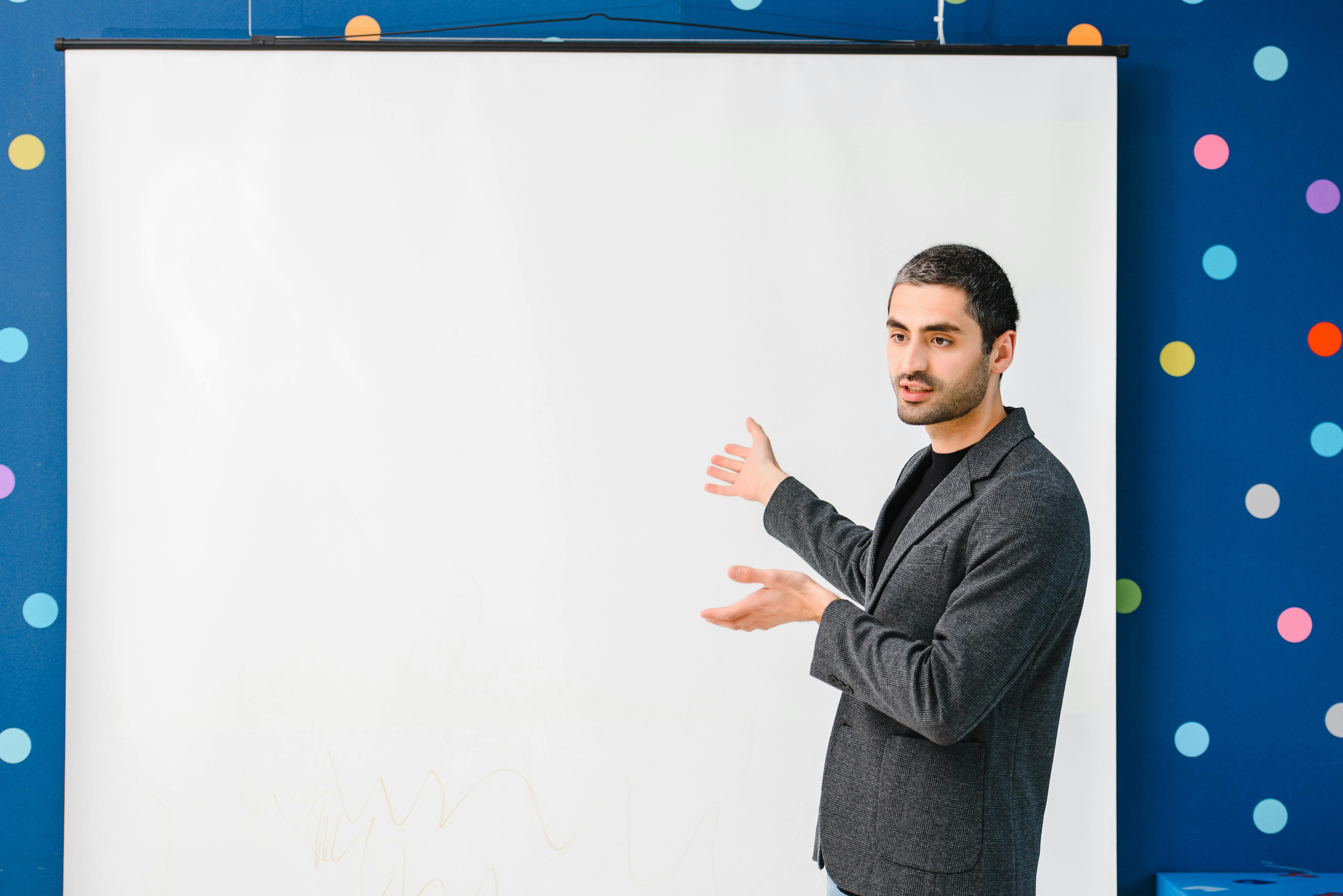 A Man in Gray Blazer Standing Beside the White Board