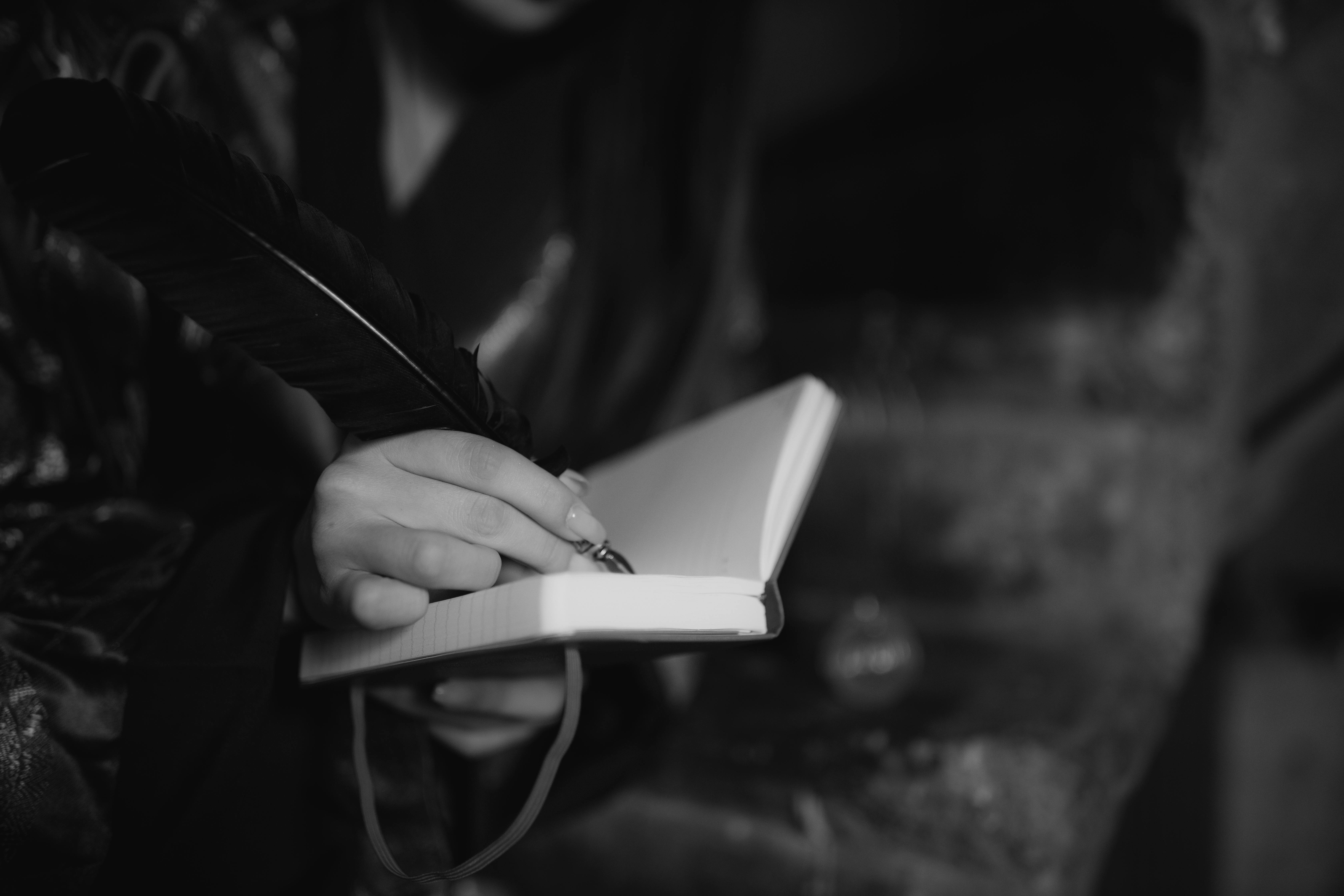 Grayscale Photo of a Person Writing with a Quill