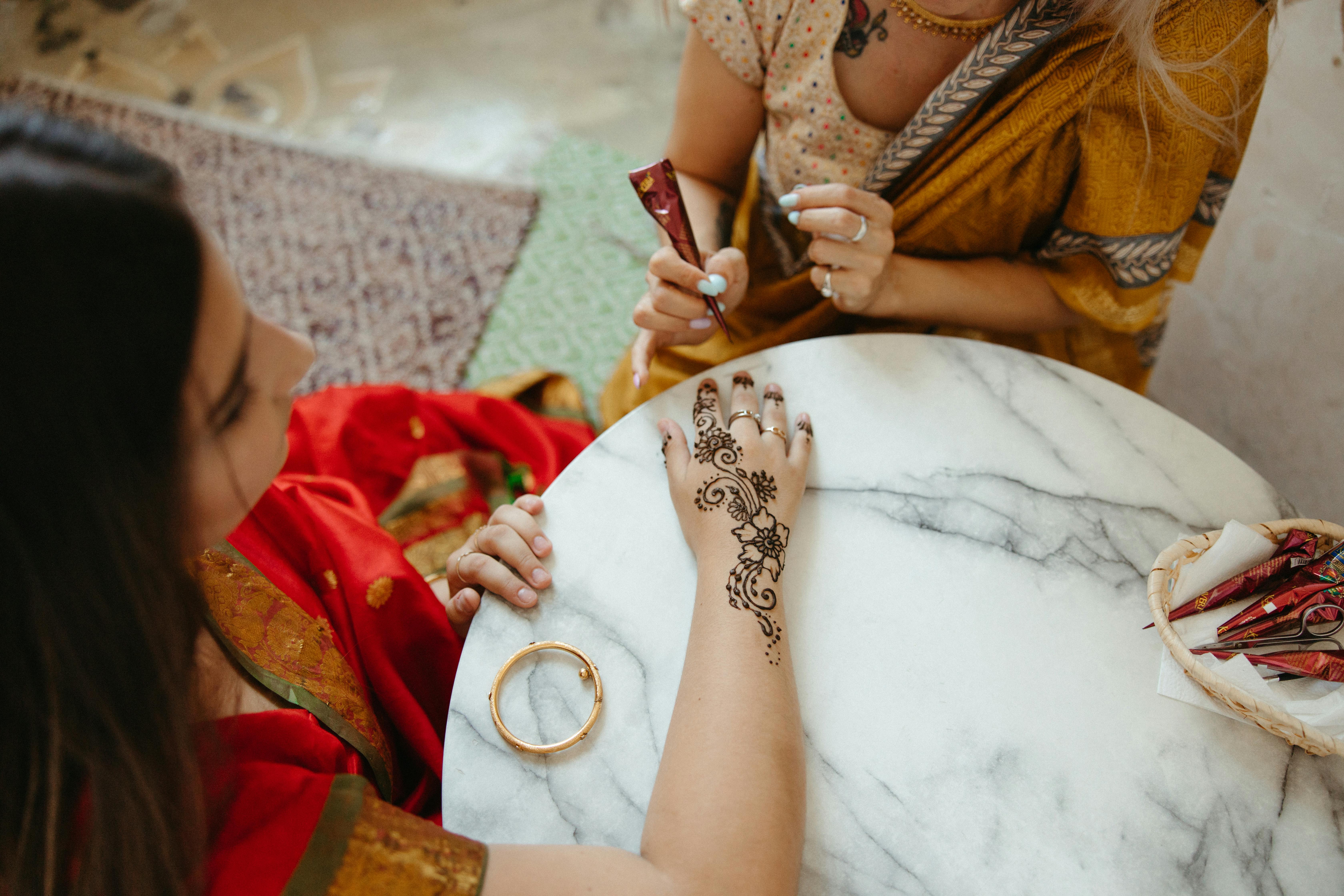 Artist Painting a Henna Tattoo on a Hand of another Woman