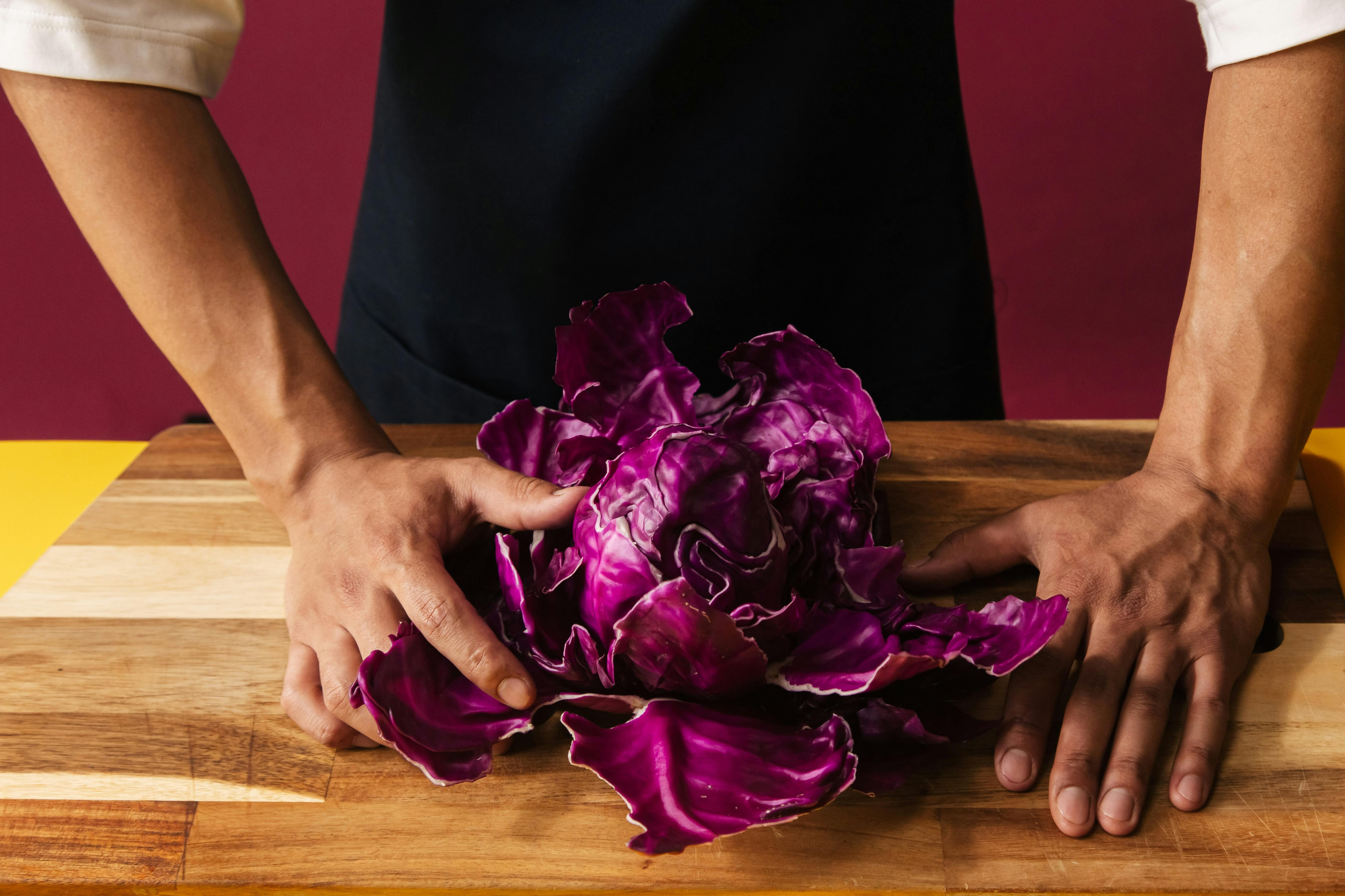 Close-Up Shot of a Person Holding a Fresh Red Cabbage on Wooden Cutting Board