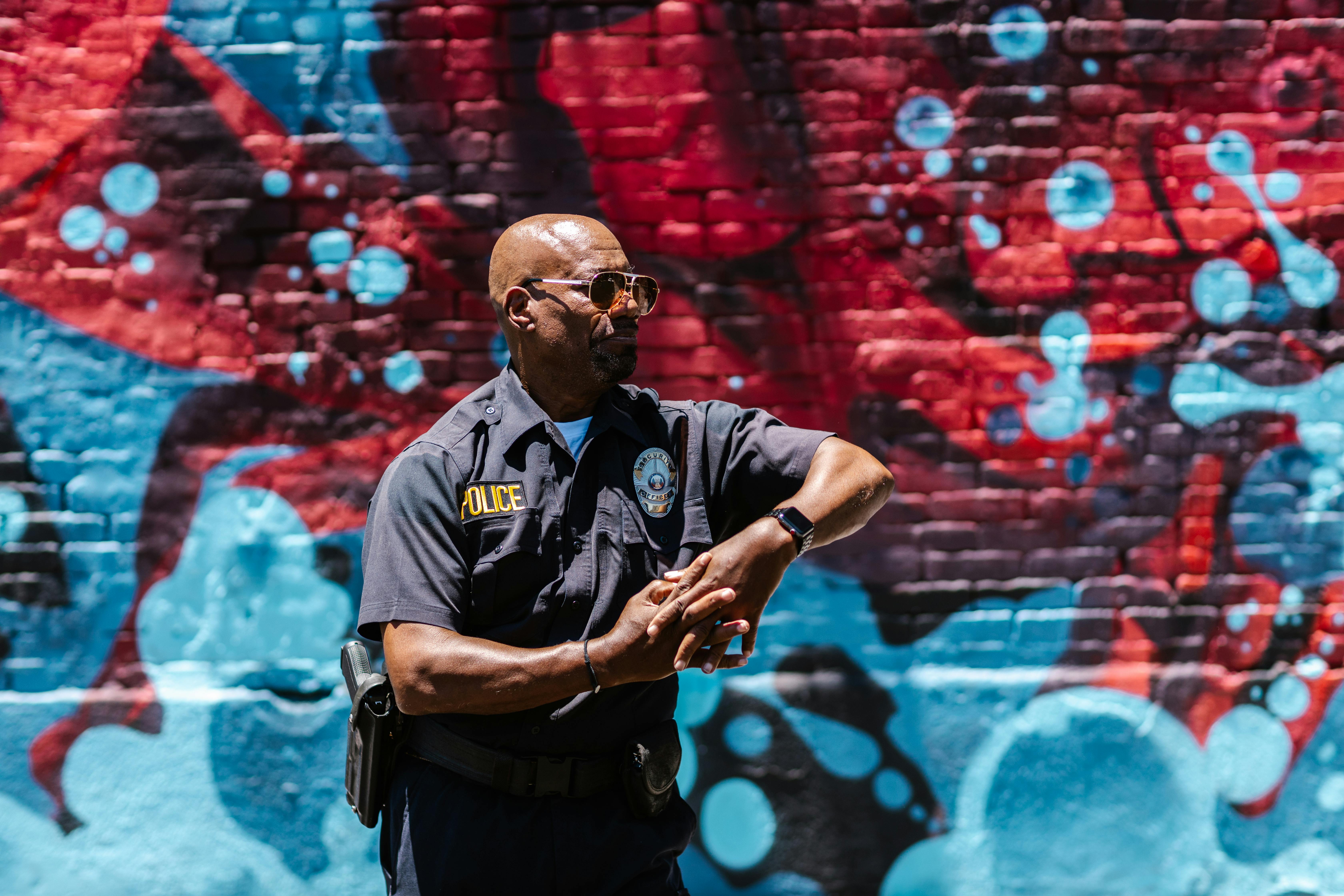 A Man in Uniform Wearing Sunglasses Standing Near the Brick Wall