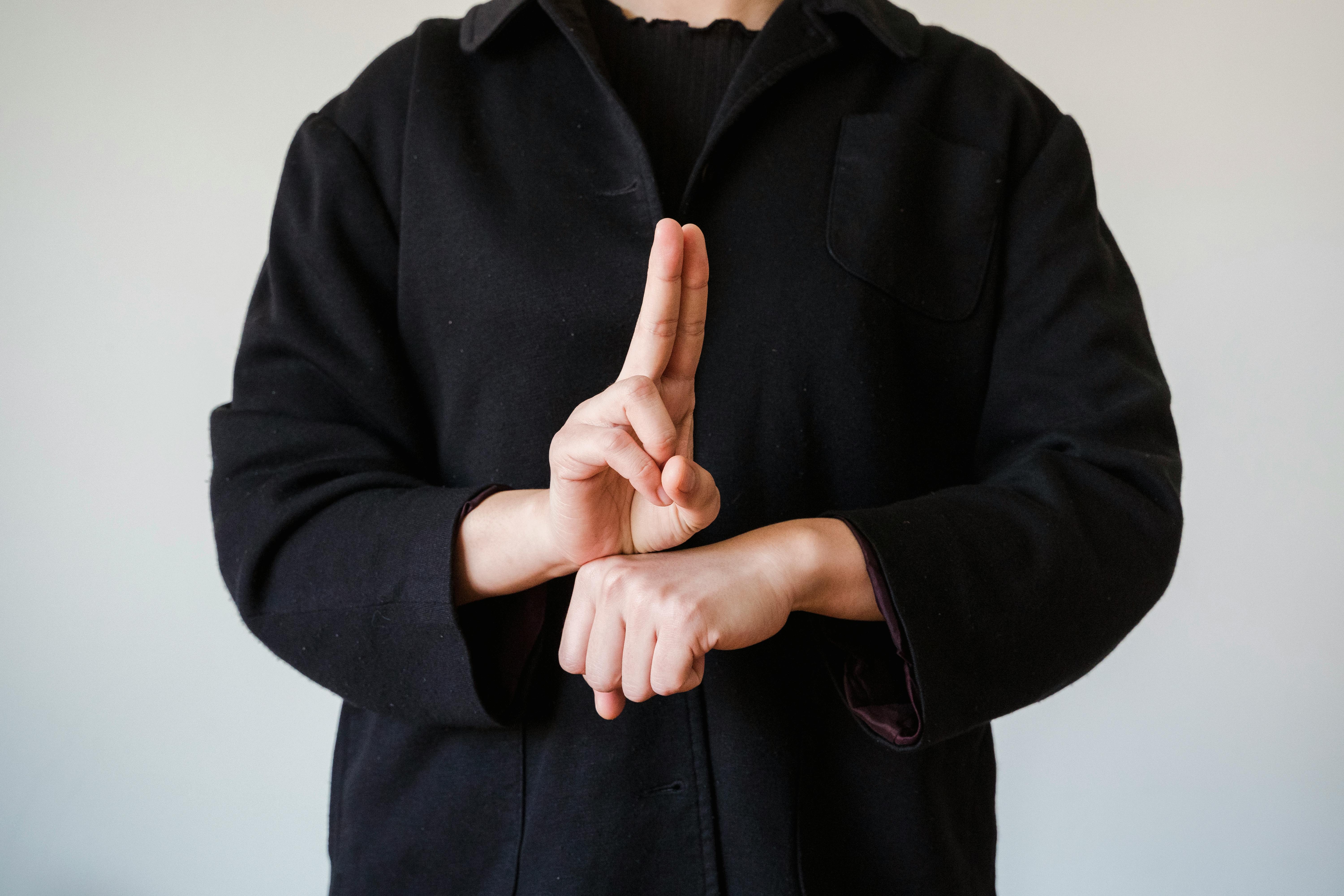 Man in a Black Coat Showing a Sign in a Sign Language