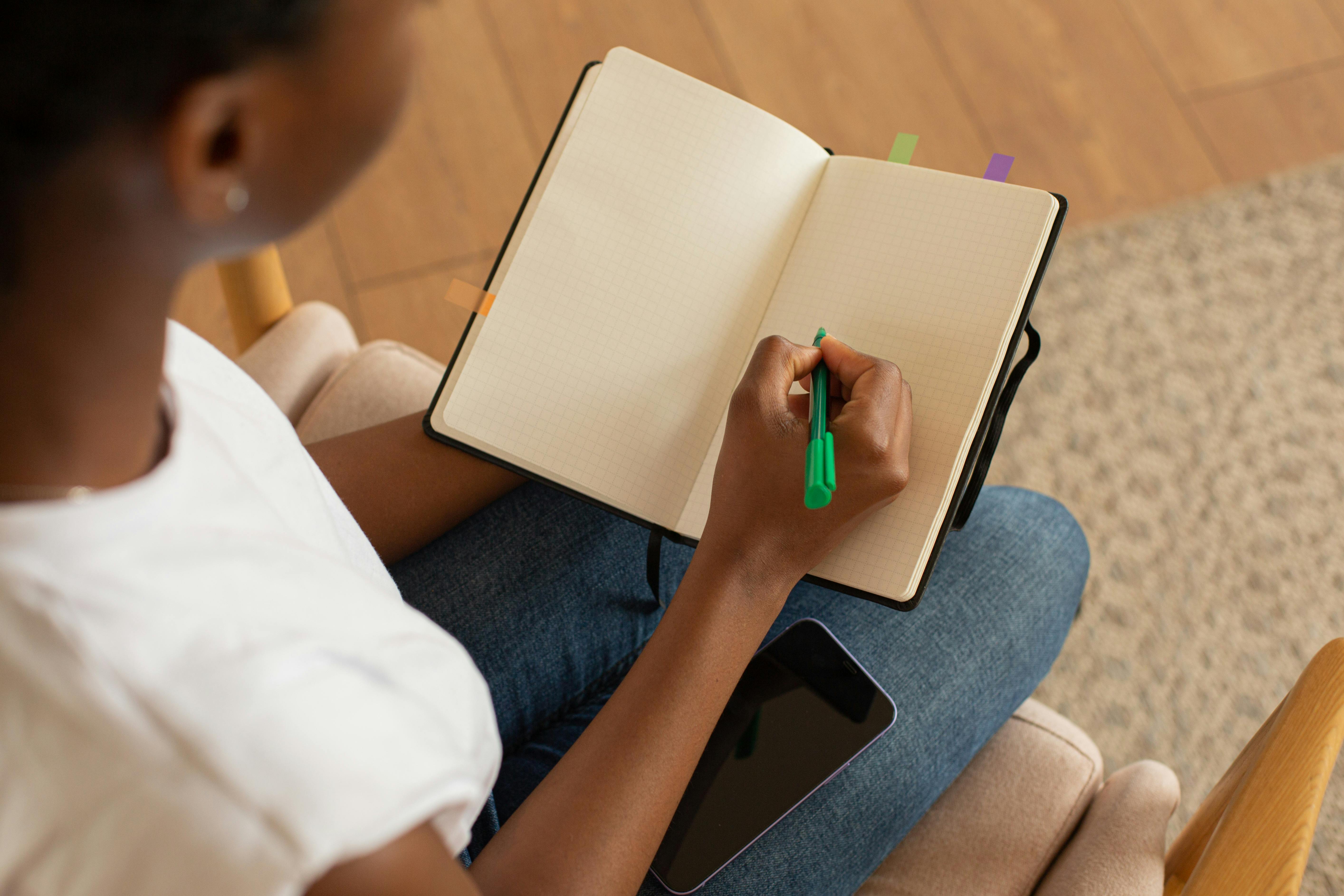 Person Holding a Notebook and a Green Pen