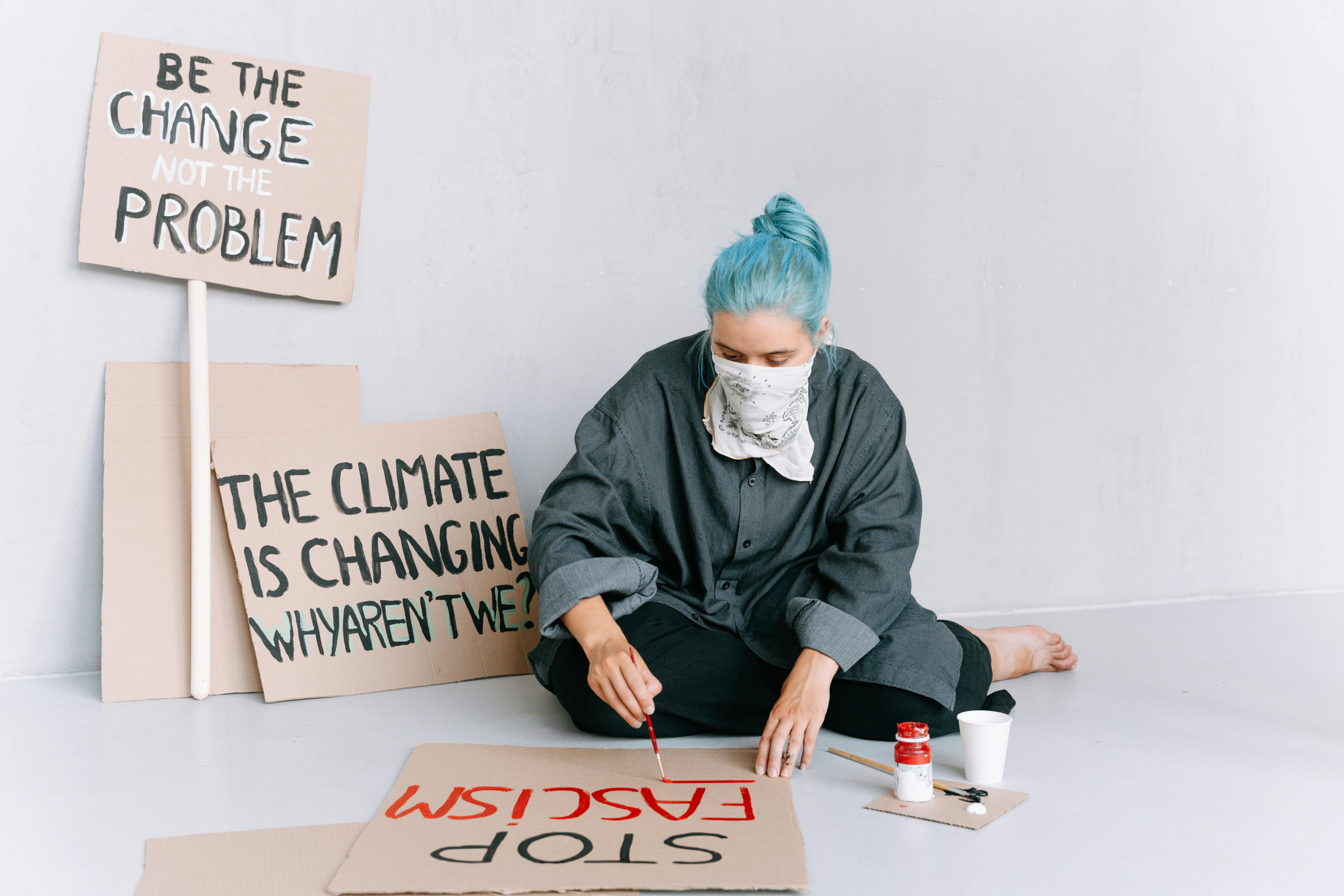 A Woman Sitting on the Floor Writing Protests on a Placard