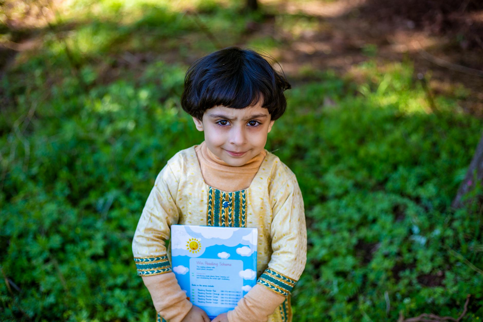 A Cute Kid Smiling While Holding a Book