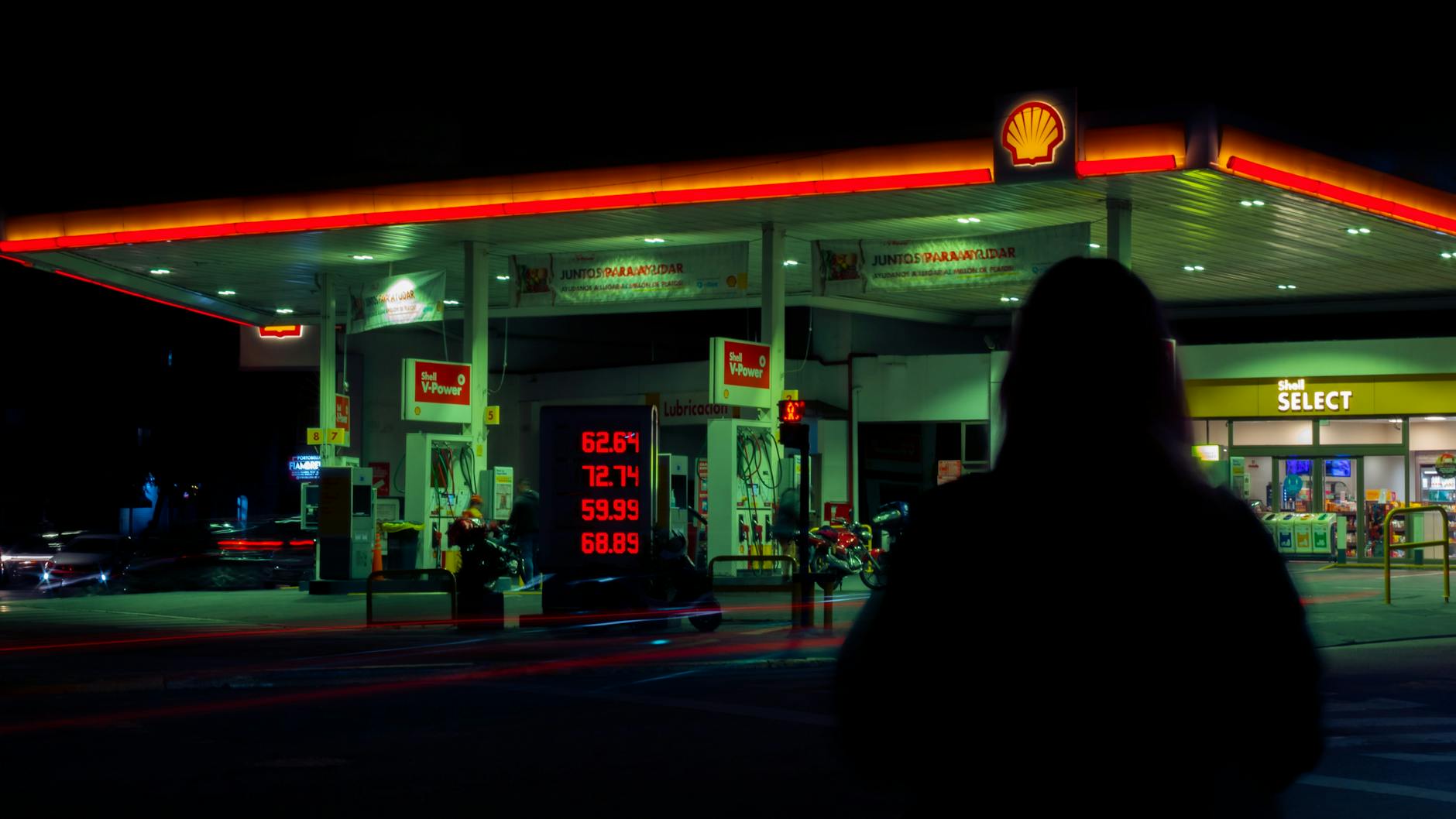 Silhouette of Person Against Gas Station in Night