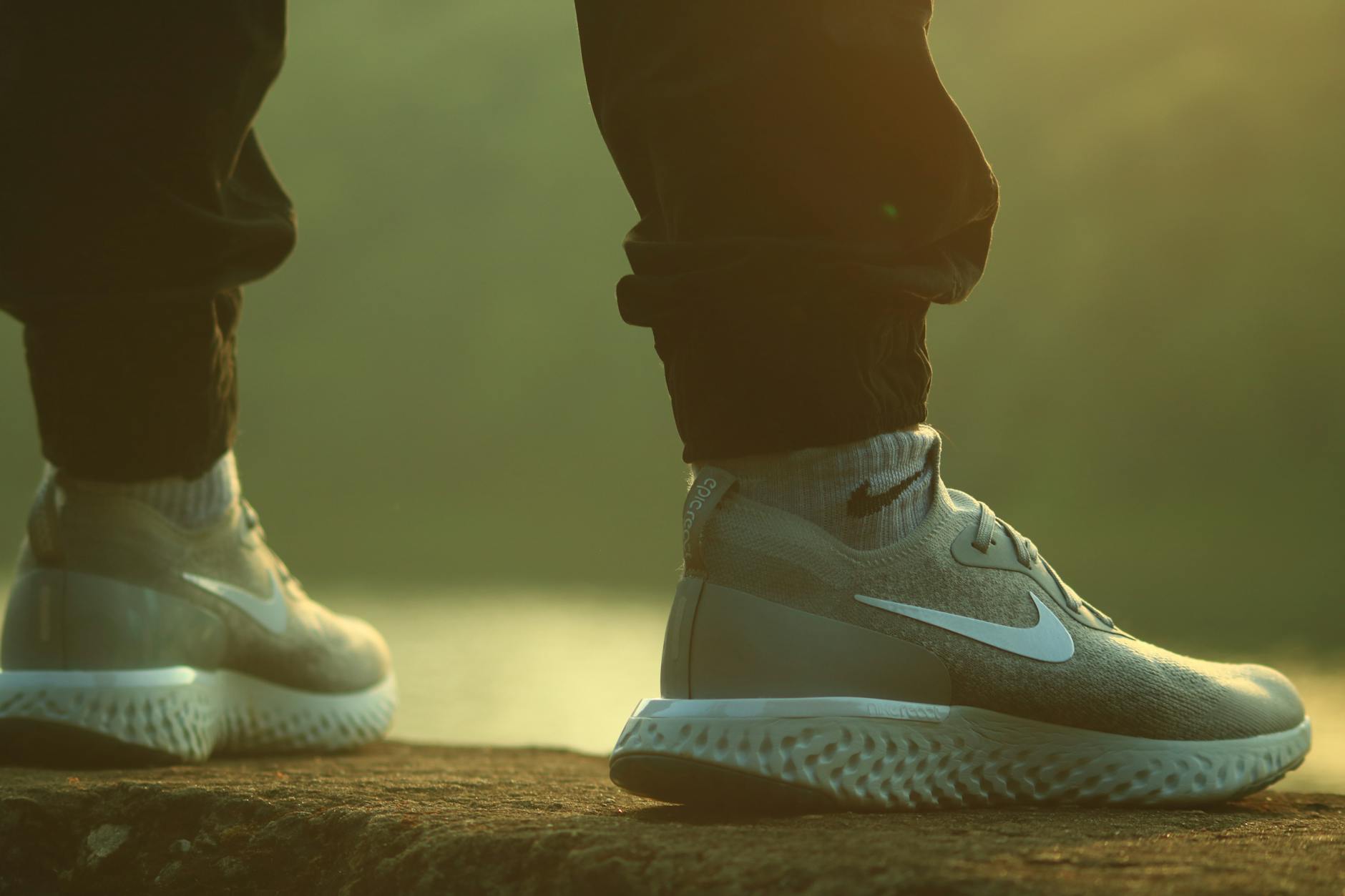 Standing Person Wearing Black Jogger Pants and Gray-and-white Nike React Running Shoes on Concrete Ground