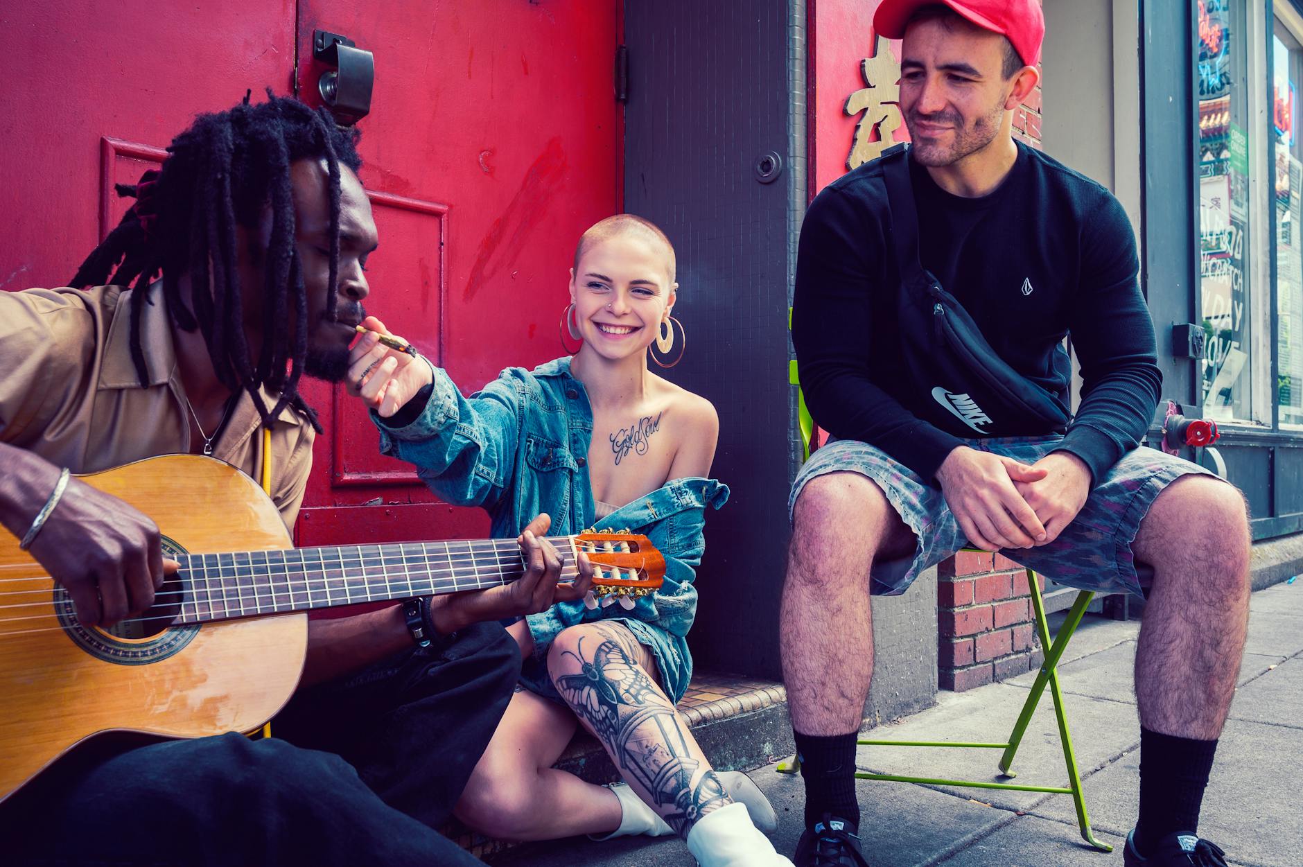 Man Playing Guitar Near Woman Wearing Denim Jacket and Man Sitting on Chair