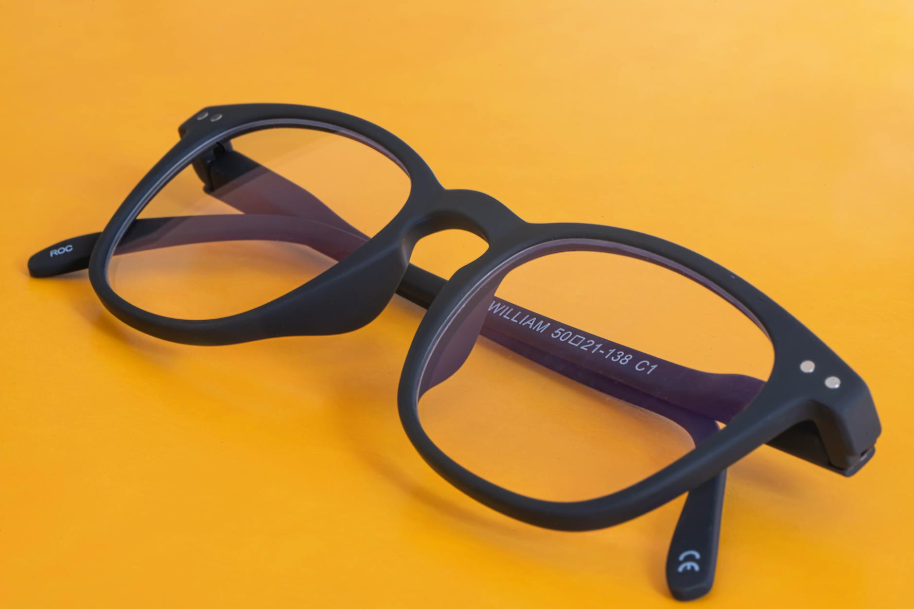 Modern black eyeglasses showcased on a vibrant orange backdrop with visible branding.