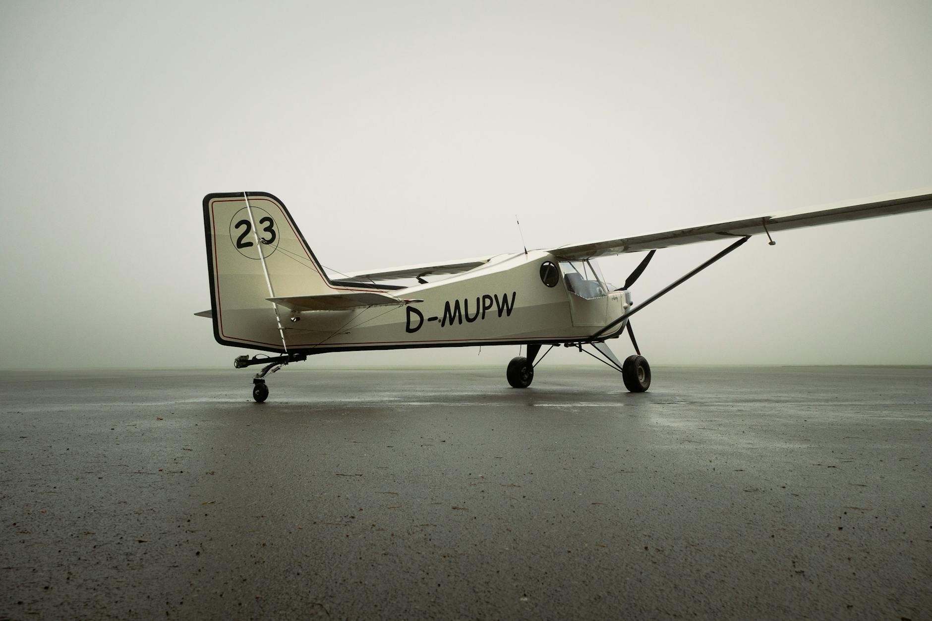 Vintage single-engine aircraft parked on a misty runway, foggy day.