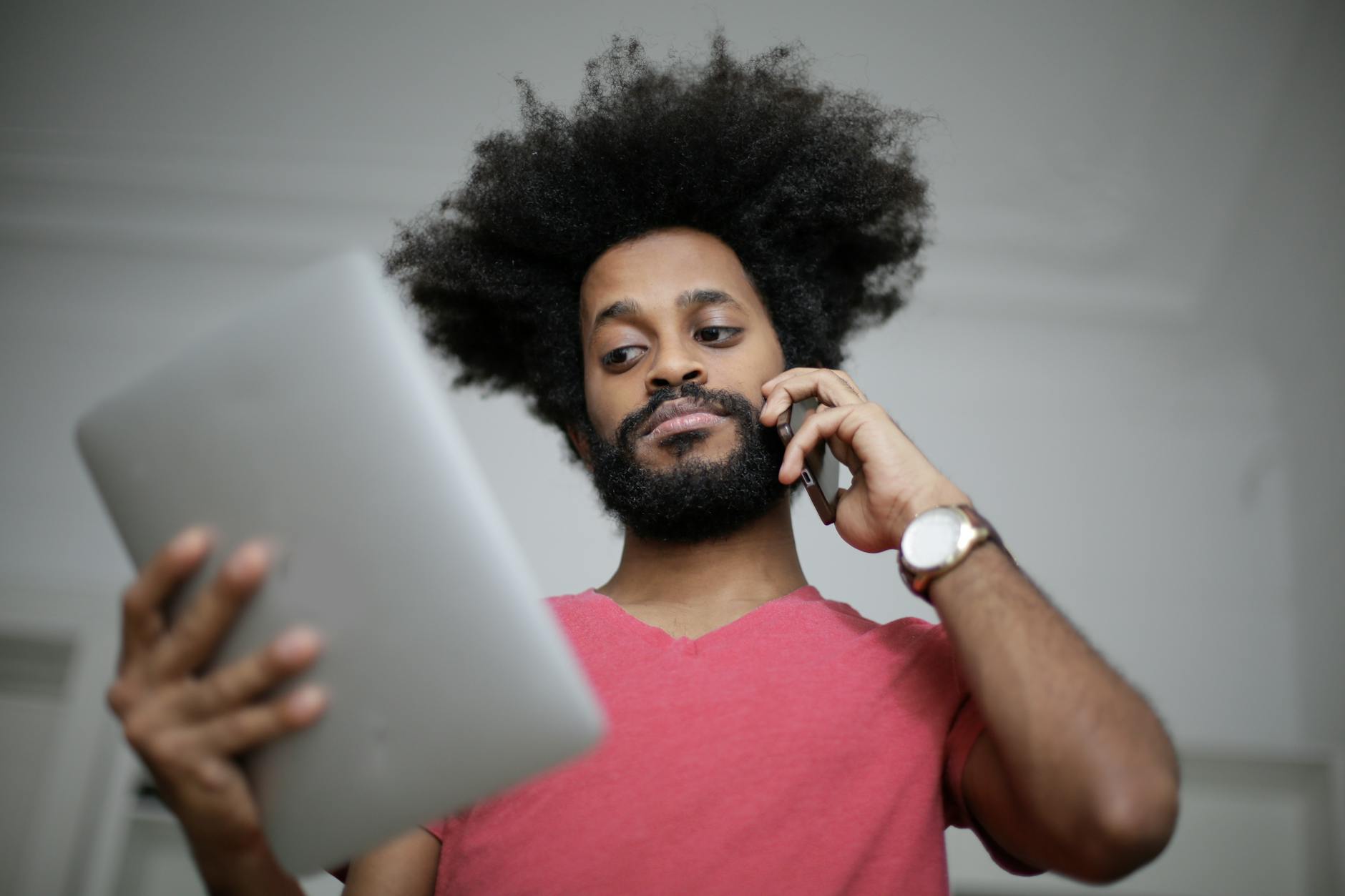 Man in Red Crew Neck T-shirt Looking on His Tablet and Making a Call