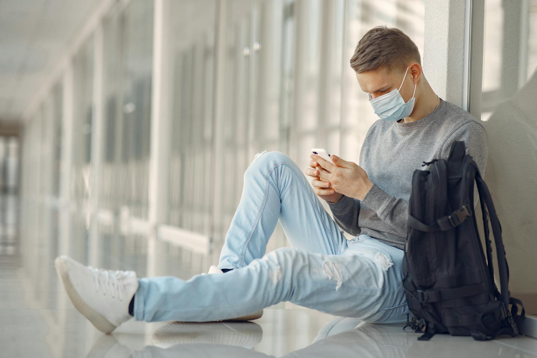 Man in Gray Sweater and Denim Pants Sitting on White Floor