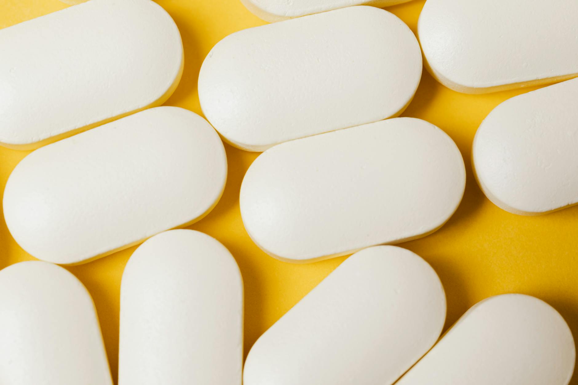 From above closeup of white ellipse-shaped medical pills placed on bright yellow surface