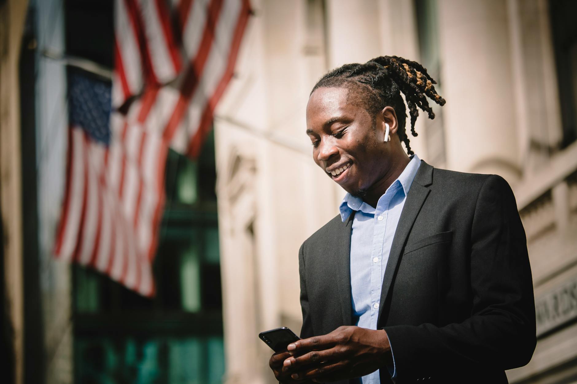 Positive young black entrepreneur using mobile on street and smiling