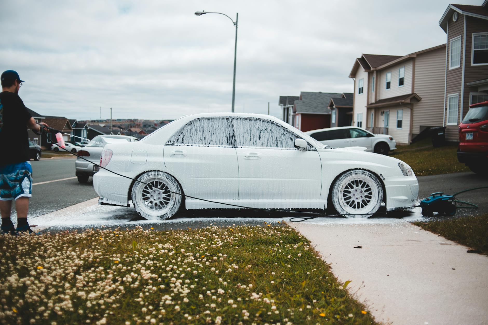 Foamed car on driveway and sidewalk being washed by male driver at daytime