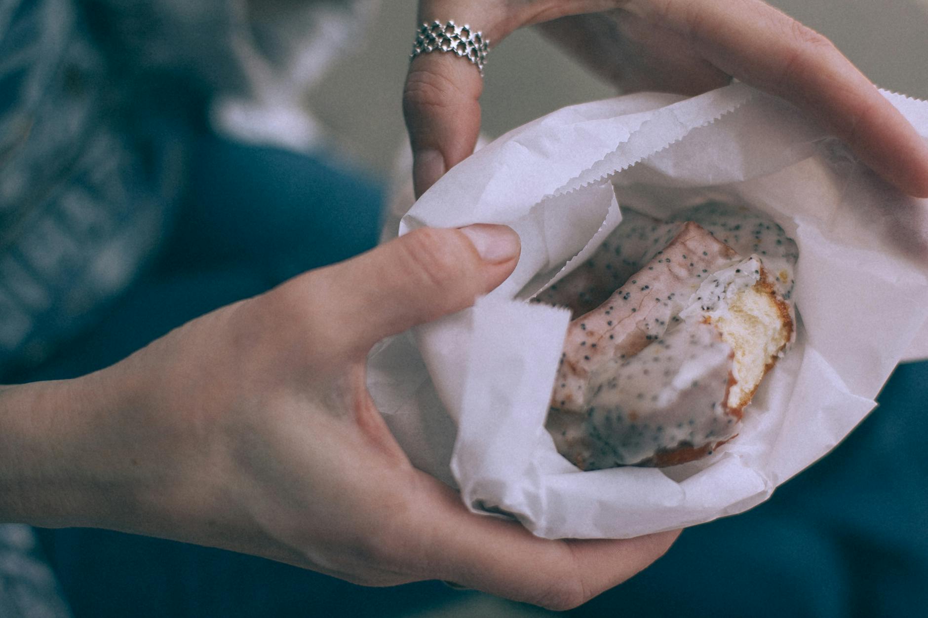 From above of crop unrecognizable person showing tasty sweet donut with glaze in organic bag on street