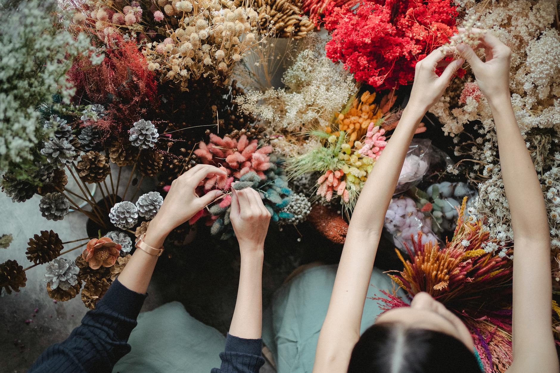 From above of crop faceless florists in aprons touching blooming flowers while working in floral shop