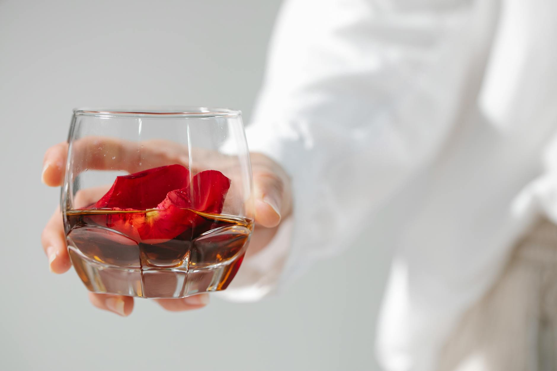 Crop person with petal on glass of drink