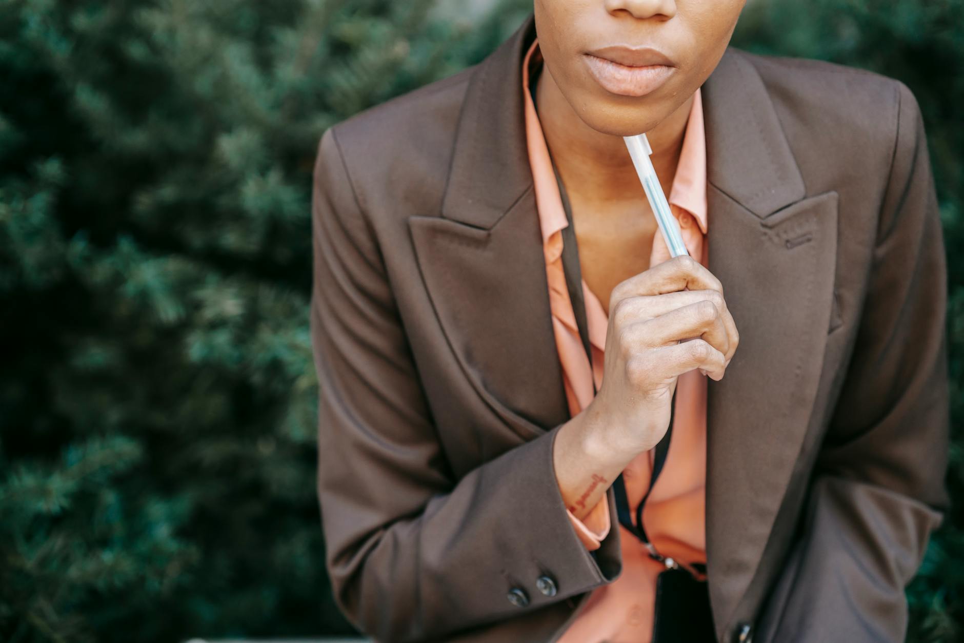 High angle of crop female entrepreneur in formal wear touching chin with pen while thinking on solution in park