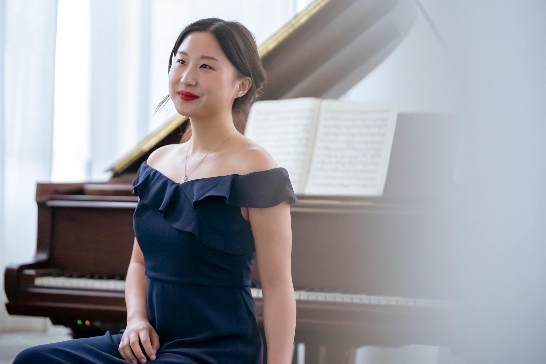 Elegant Asian female musician sitting near piano