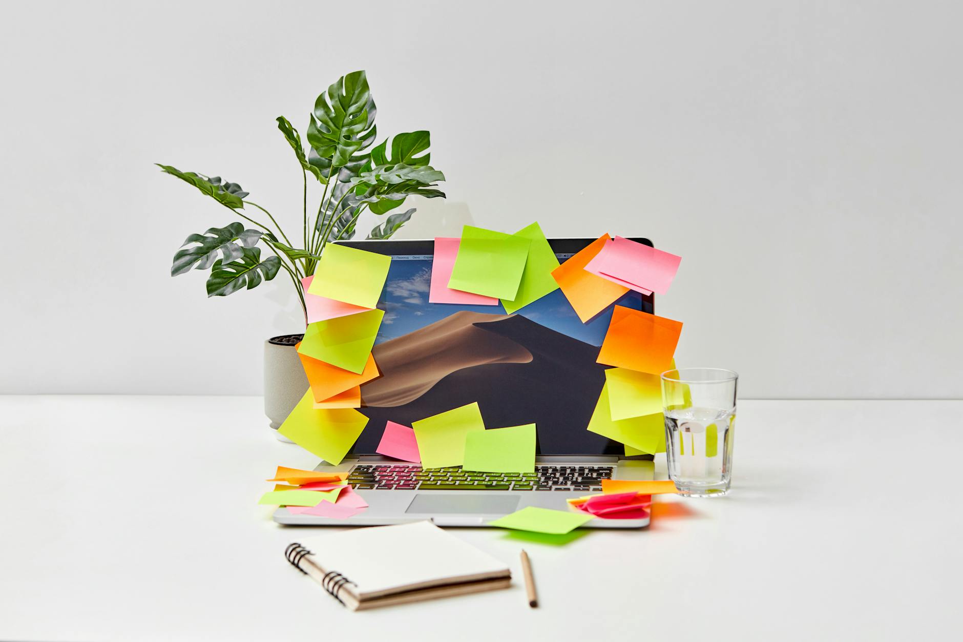 Close-Up Shot of a Laptop with Sticky Notes beside a Plant and a Glass of Water
