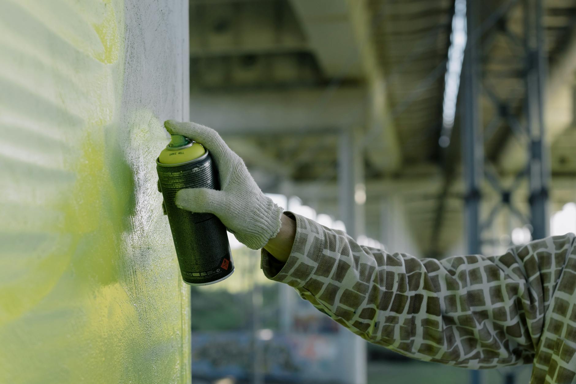 A Person's Hand Wearing Gloves Spraying Paint on Concrete Wall