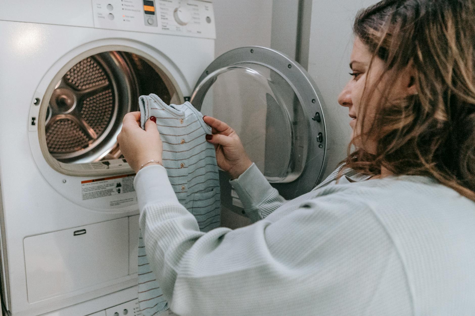 Side view of crop female in casual outfit looking at baby bodysuit before washing clothes in laundry room