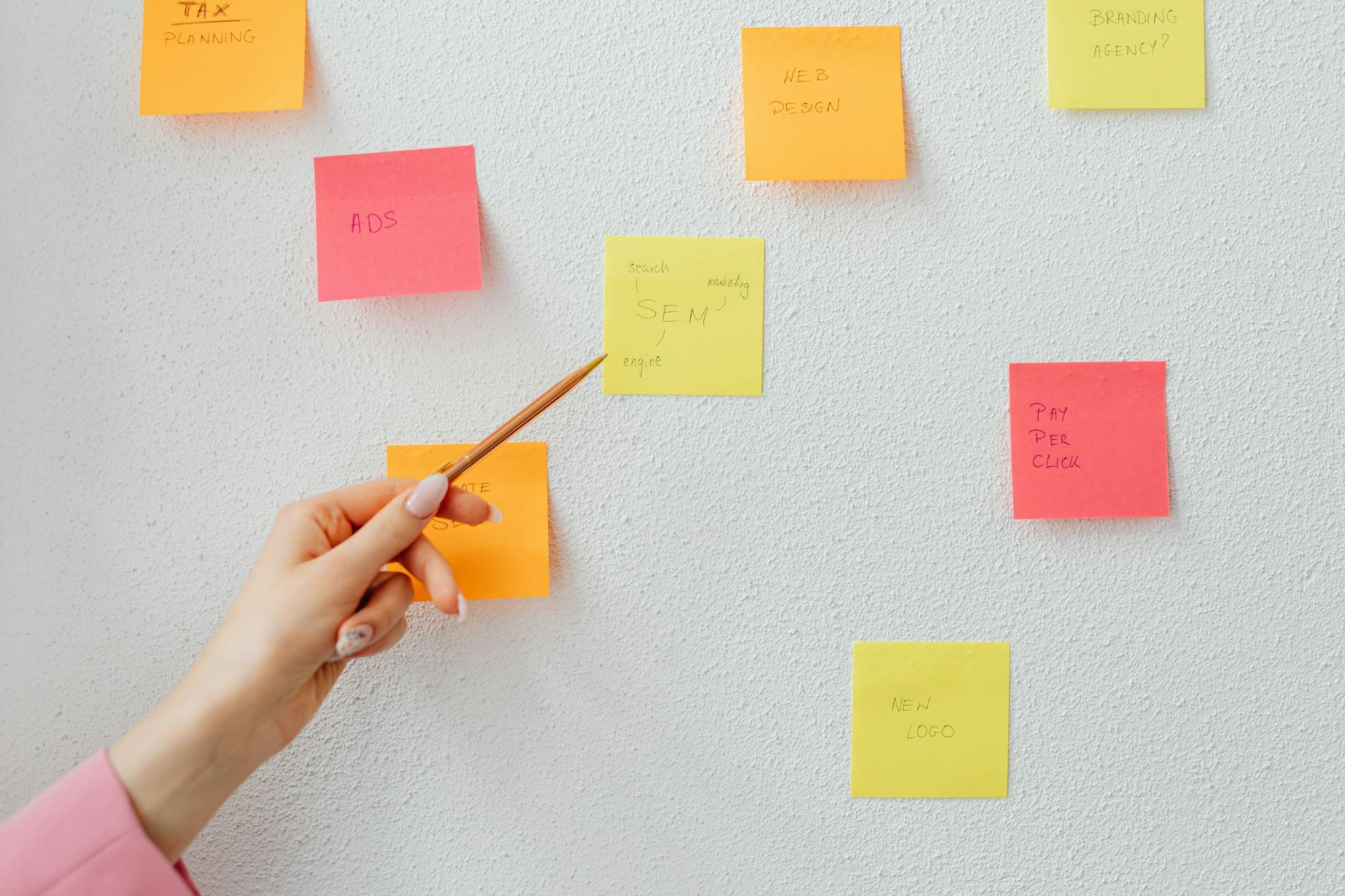 A person pointing at a sticky note on the wall using a pen.