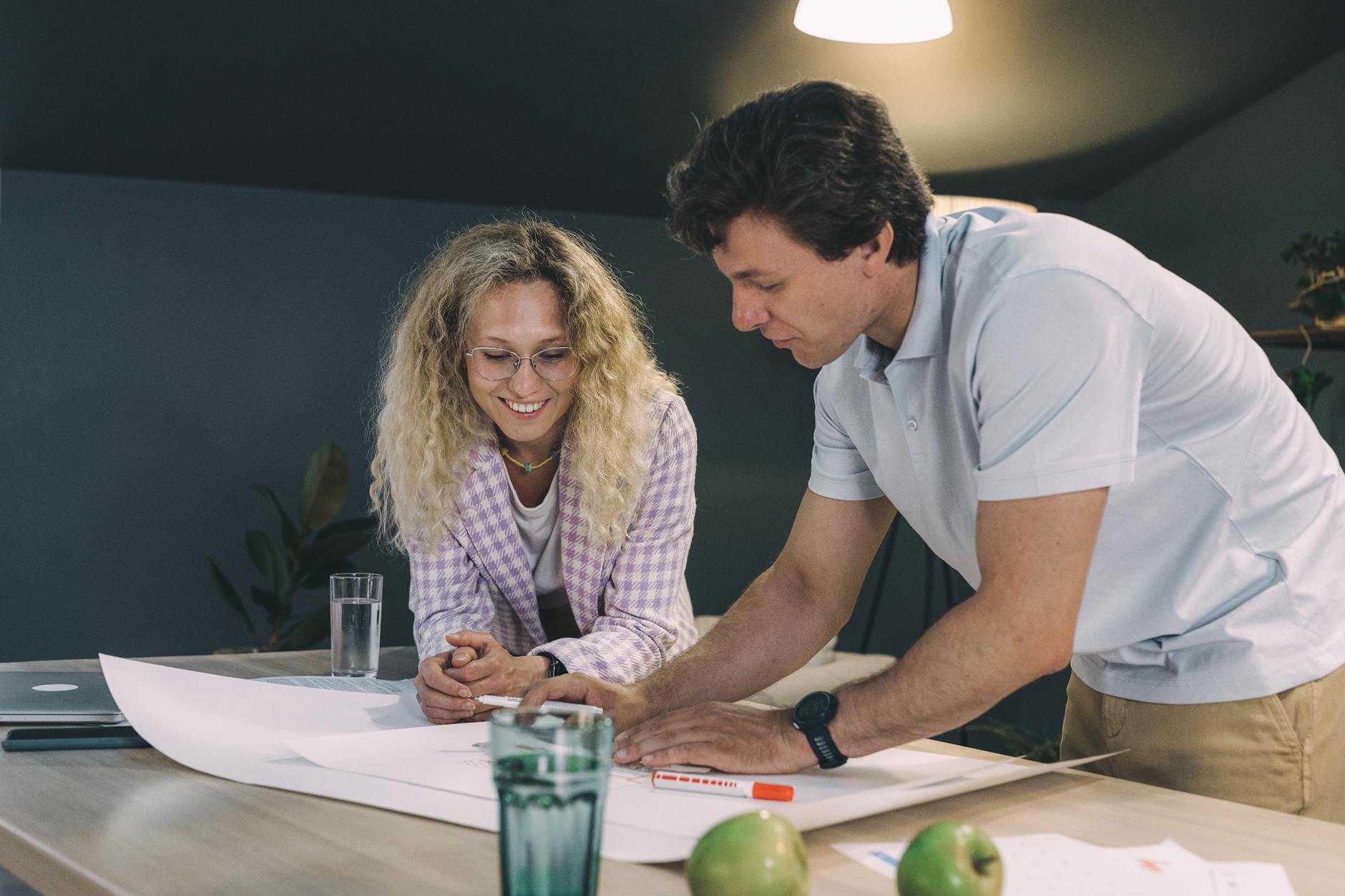 Man in White Polo Shirt Beside Woman in Checkered Coat Making a Floor Plan