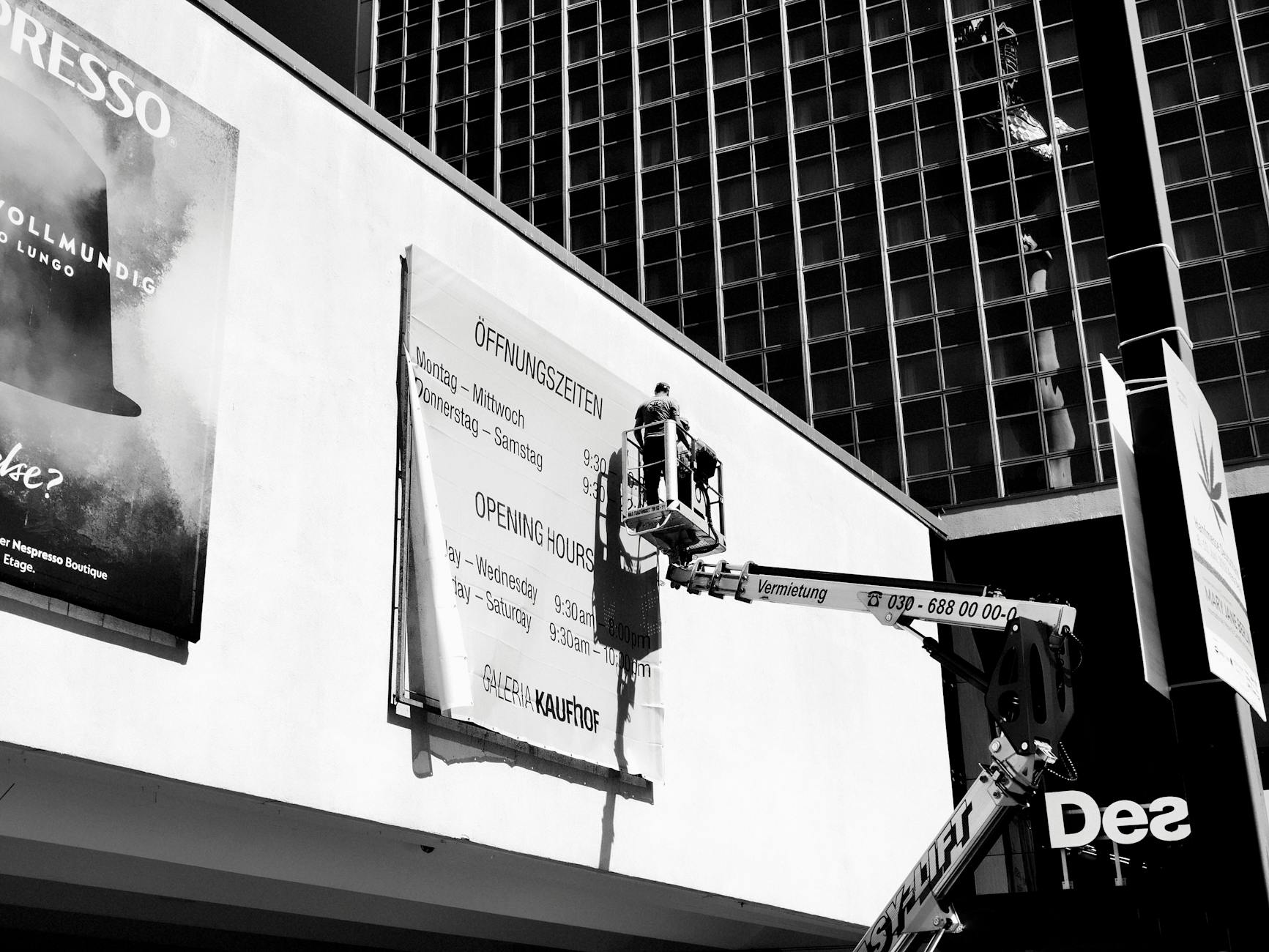 Grayscale Photo of Worker on an Aerial Lift Fixing a Billboard